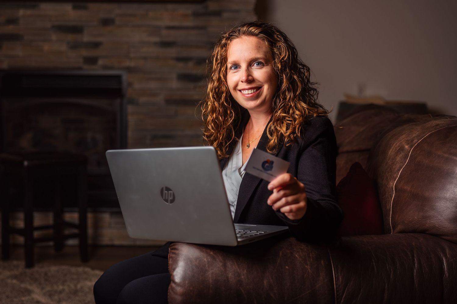 Person smiles while using laptop on comfortable leather couch in rustic room.