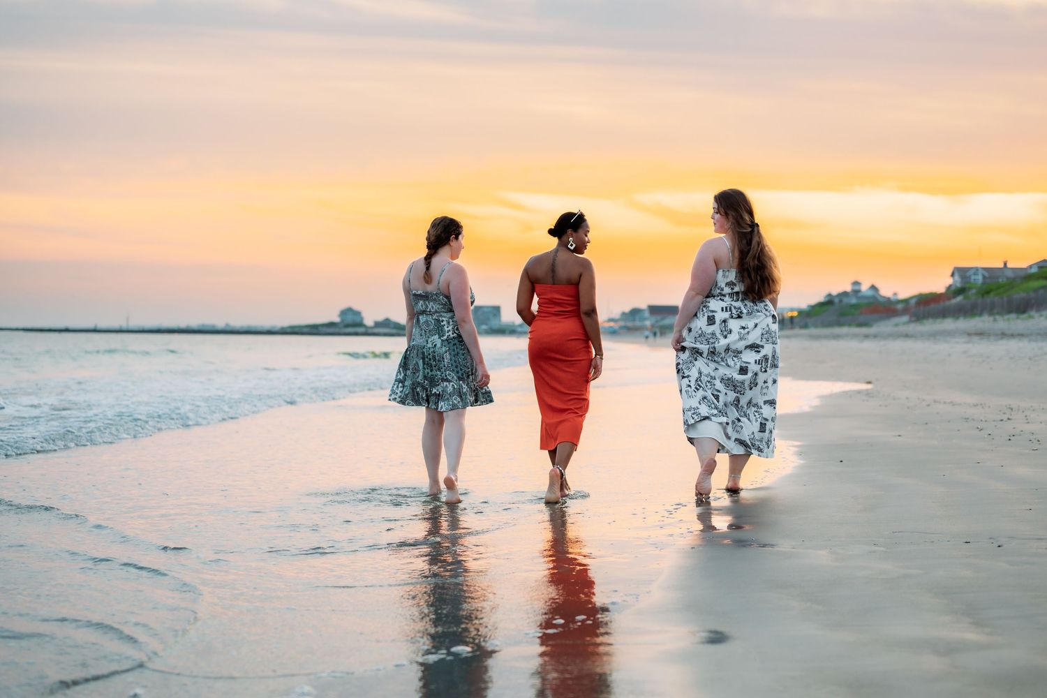 Three figures walk along a beach at sunset casting long shadows on the sand.
