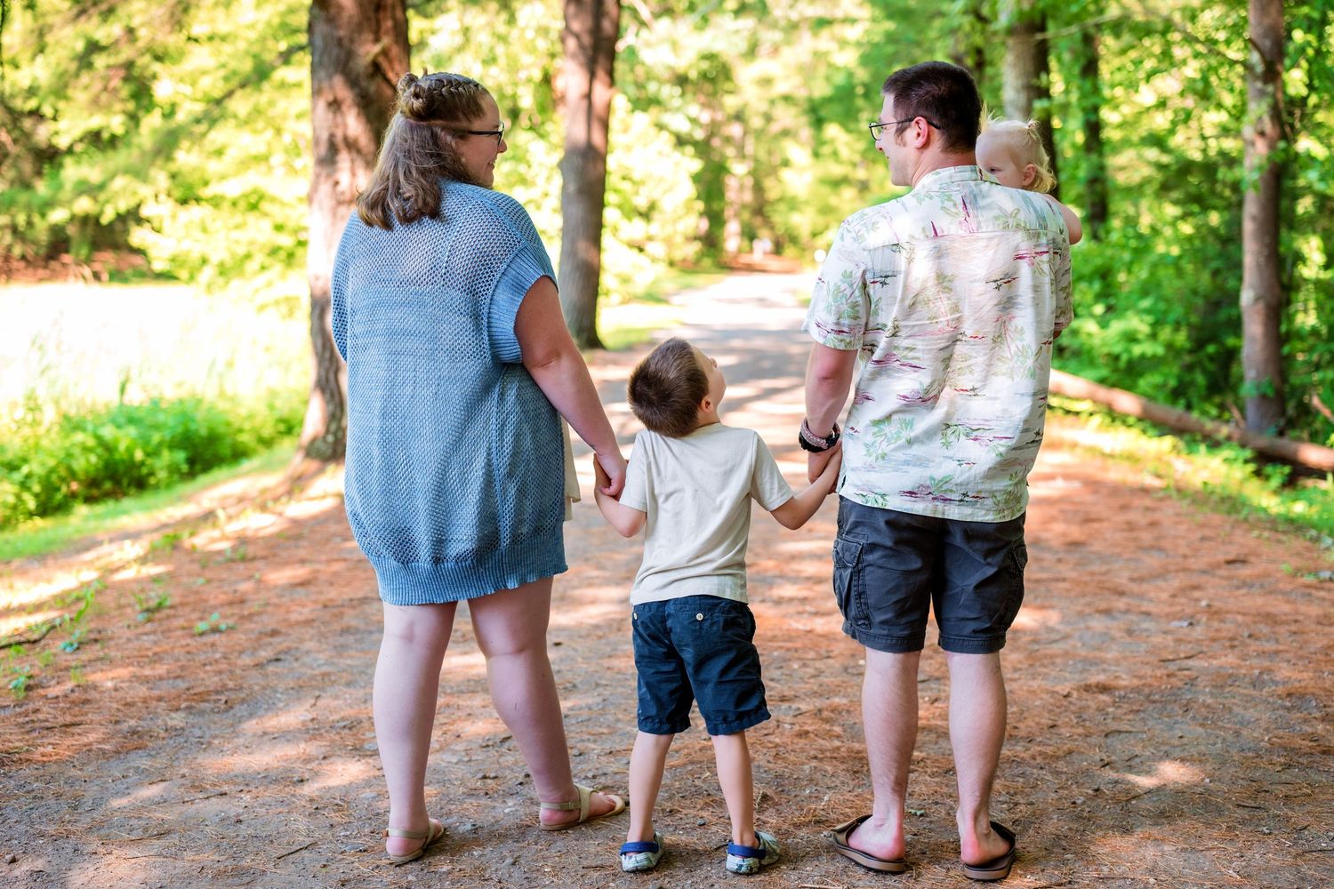 Family walking together on a wooded trail through a lush green forest on a sunny day.