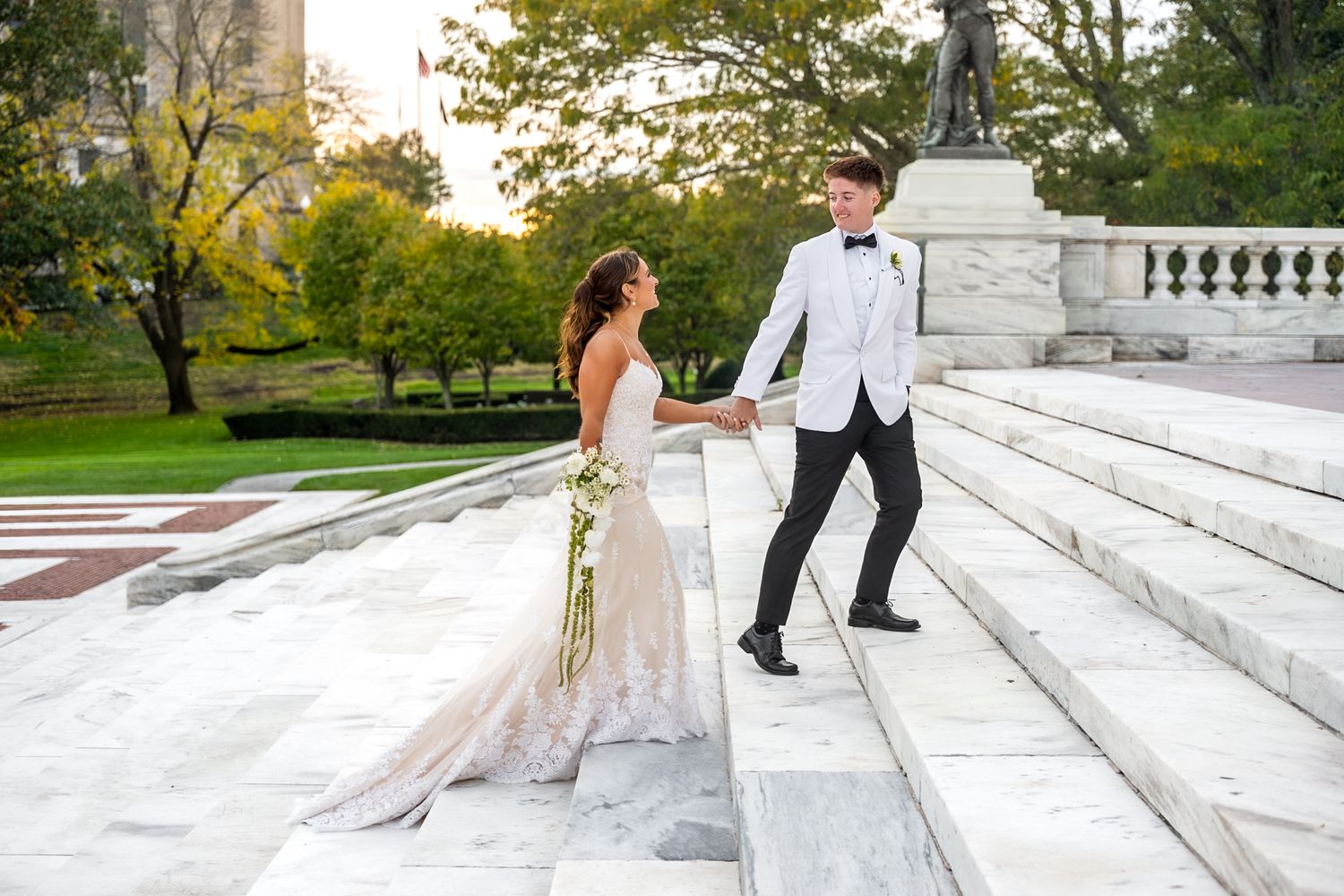 A couple sits together on elegant white marble steps during a formal photo session in a scenic outdoor setting.