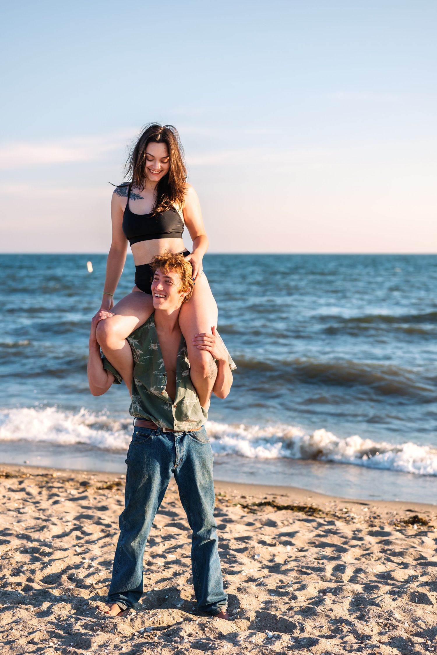 Playful moment captured at sunset on a sandy beach with ocean waves in the background.