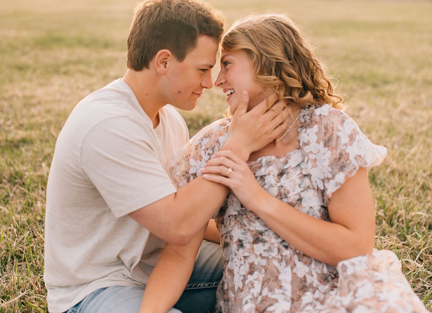 Romantic couple in casual summer attire sharing an intimate moment in a sunlit meadow.