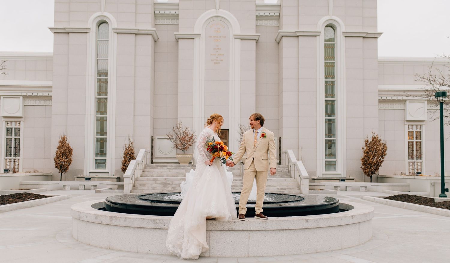 Newlyweds share a moment on circular steps outside elegant white temple building.