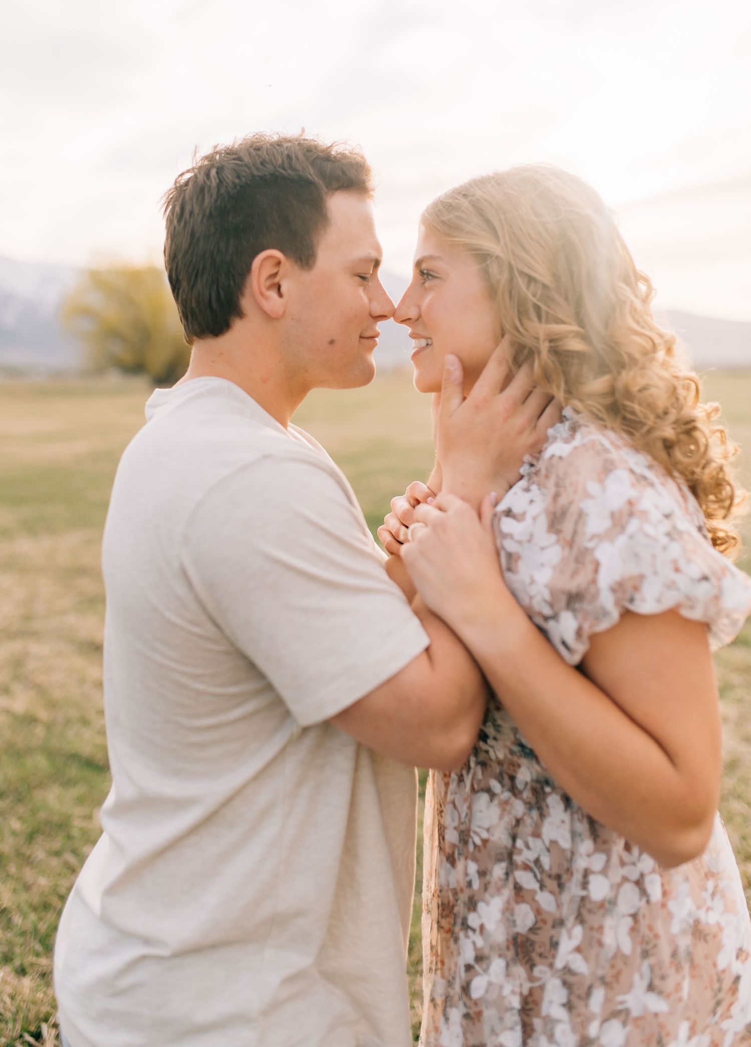 A tender romantic moment between a couple embracing in golden sunset light outdoors.