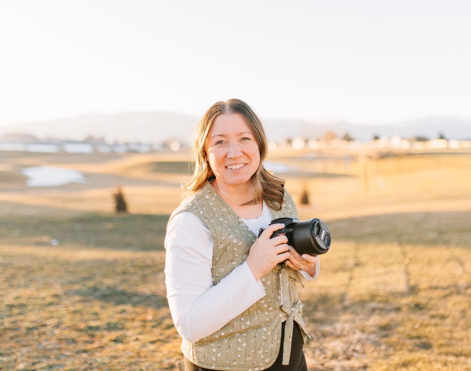 Photographer with camera stands in golden field at sunset capturing scenic landscape views.