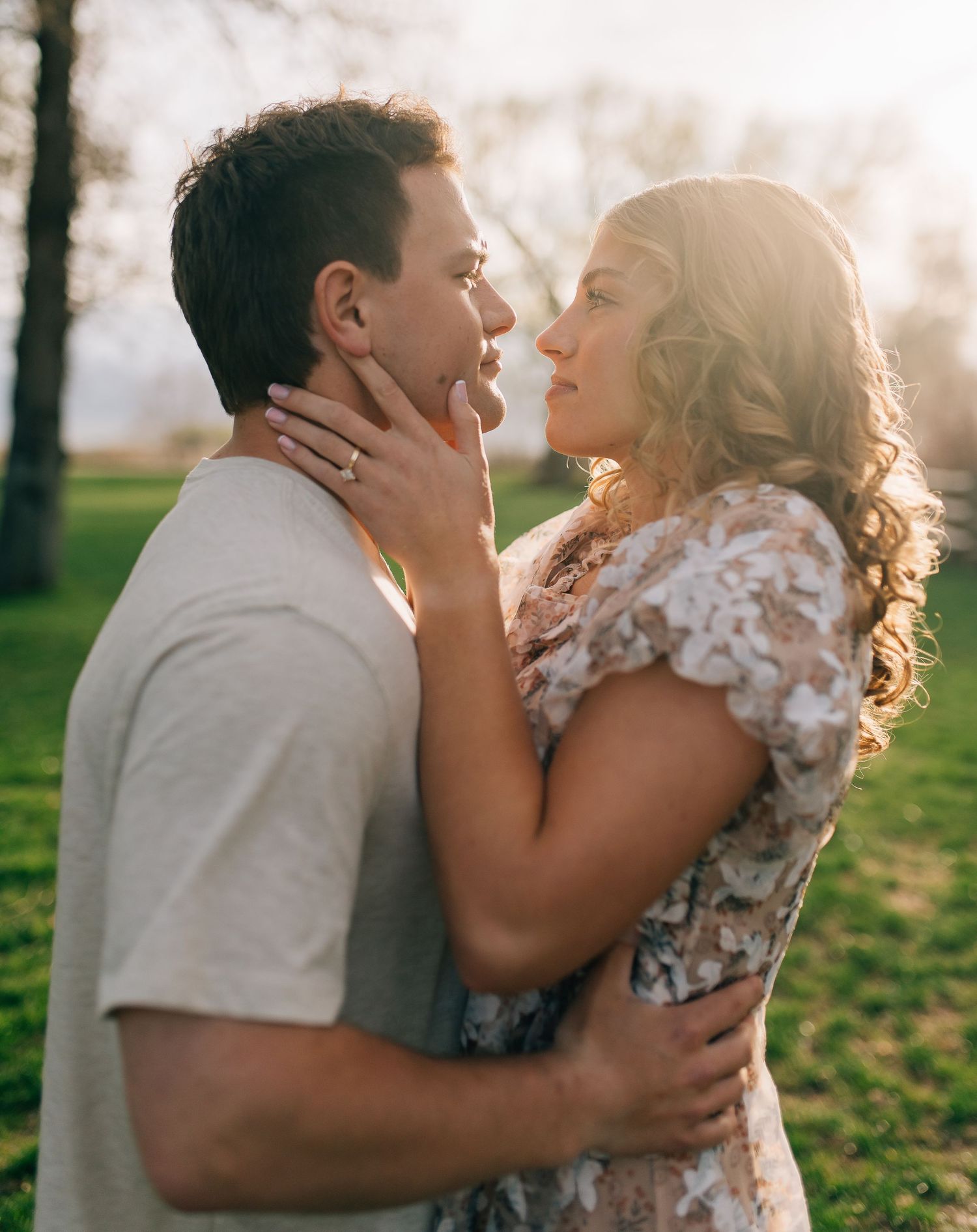 Romantic couple sharing an intimate moment at sunset in a park with golden sunlight streaming through trees.