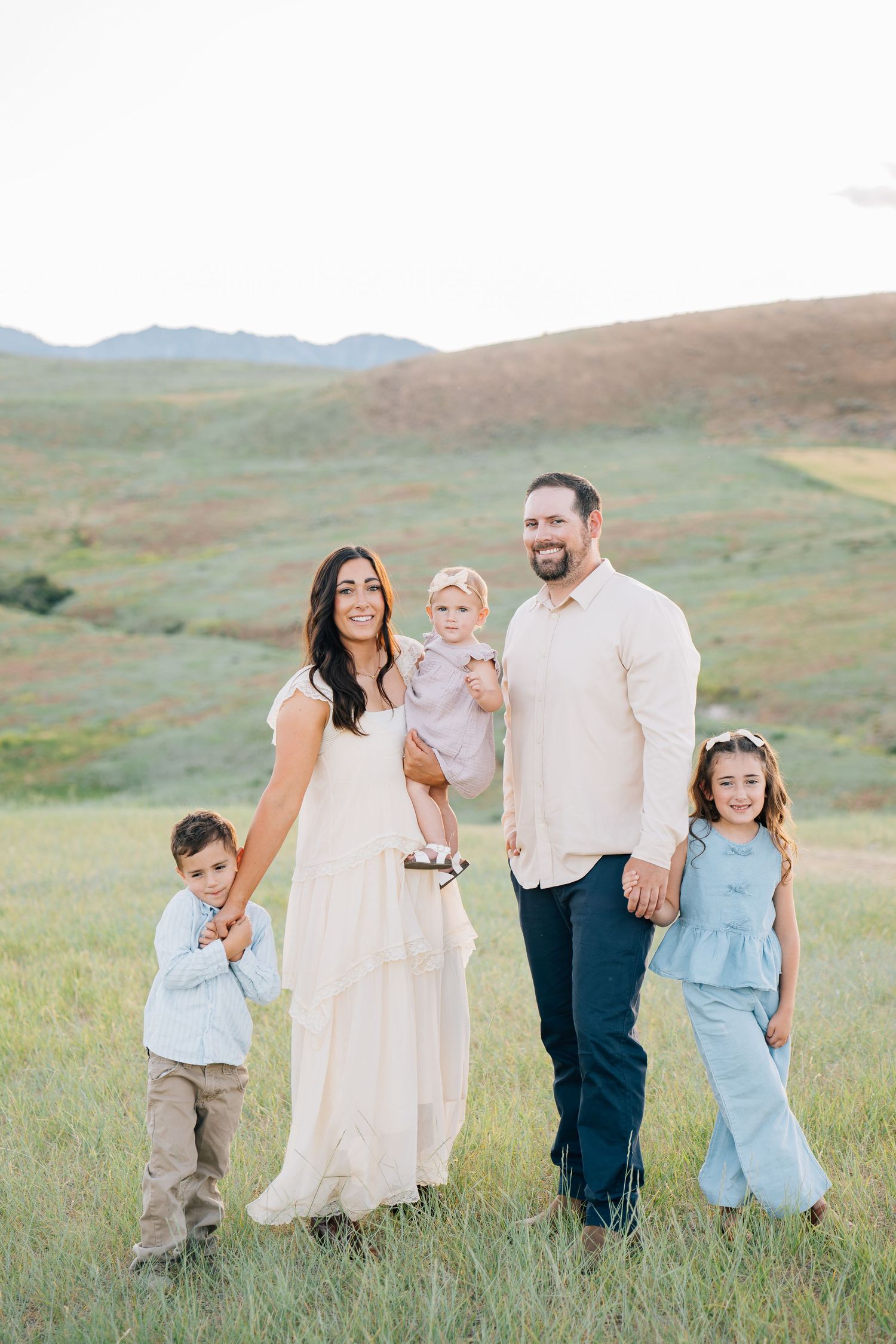 A happy family of five poses in a lush green field, with parents holding children in coordinated pastel outfits.