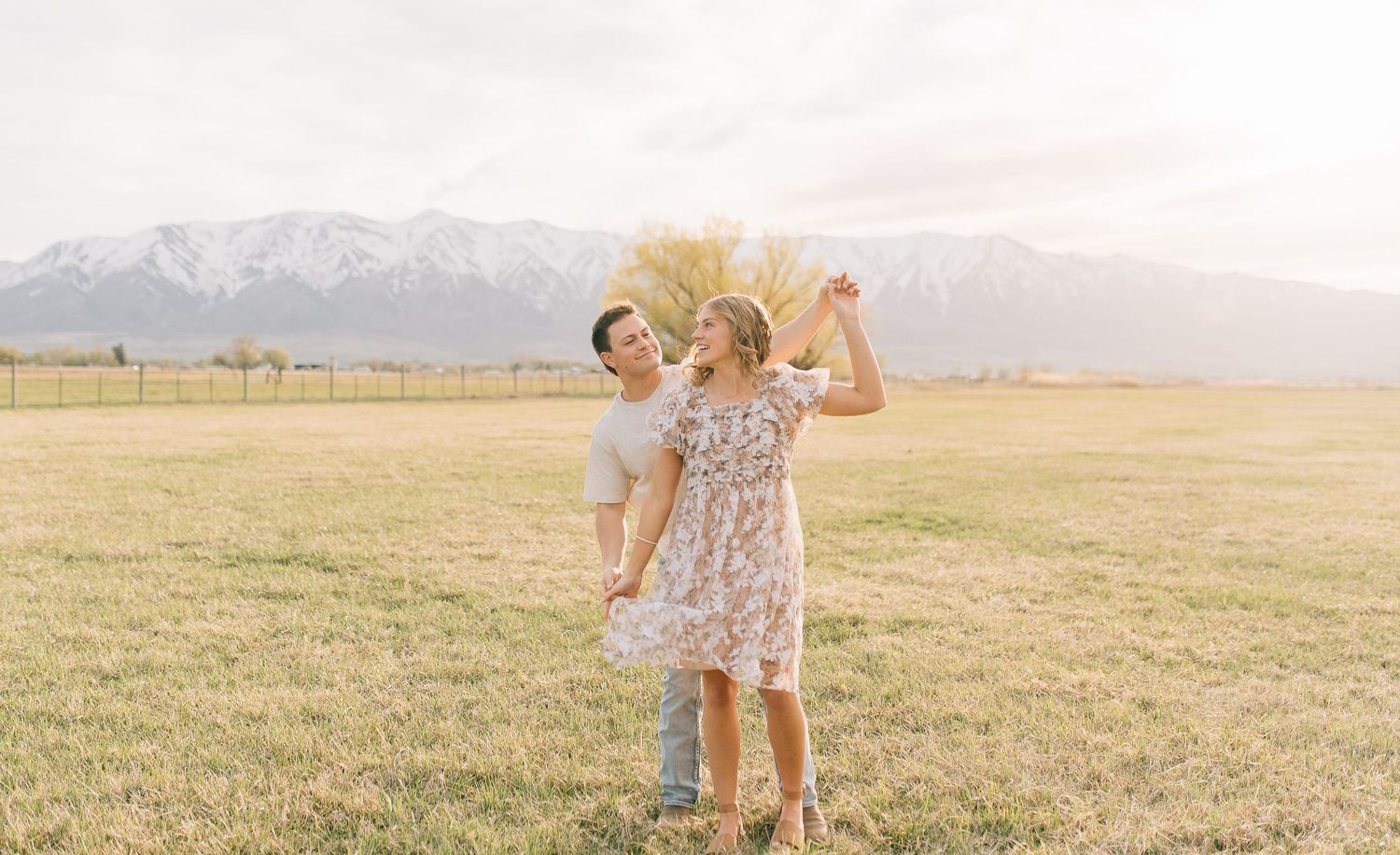People sharing a playful moment in a flowery dress against a mountain backdrop at sunset.