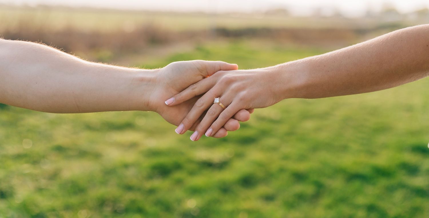 Two hands reaching out to hold each other against a blurred green grass background.