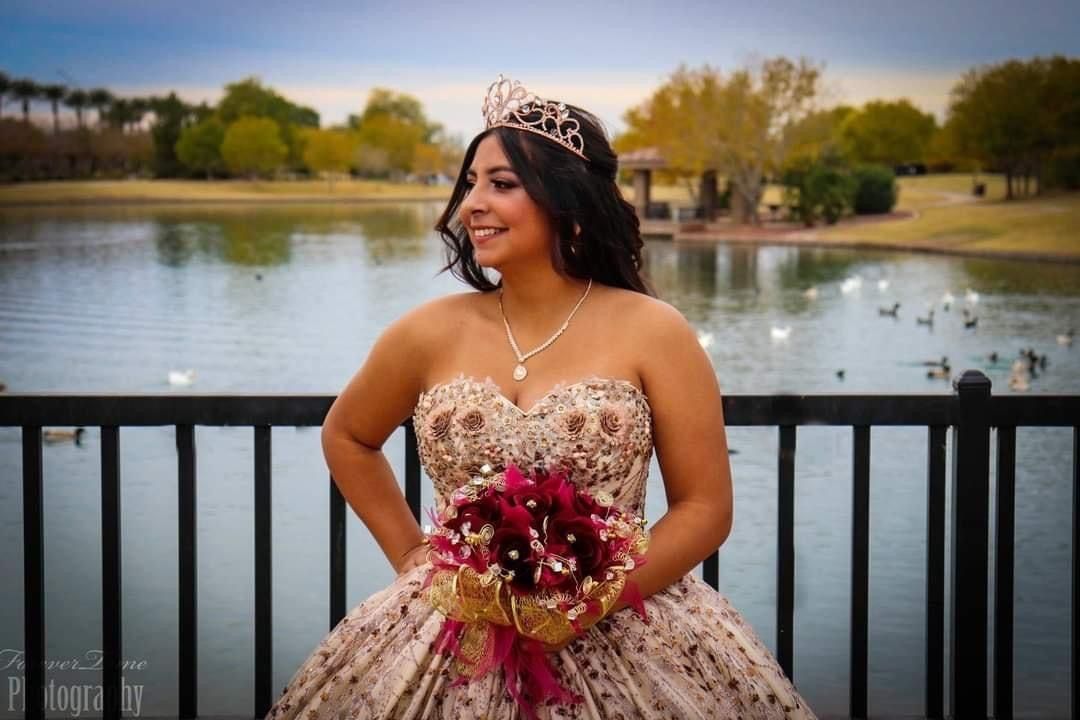 A strapless gold sequined gown sparkles by a lakeside as red and pink flowers compose a beautiful bouquet.