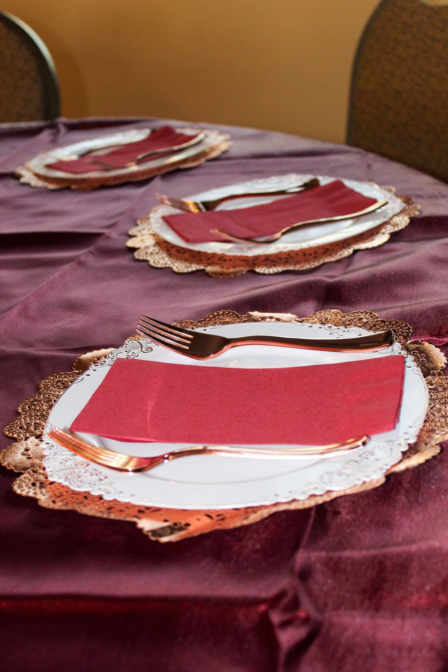 Elegant table setting with red napkins and copper charger plates on burgundy tablecloth.