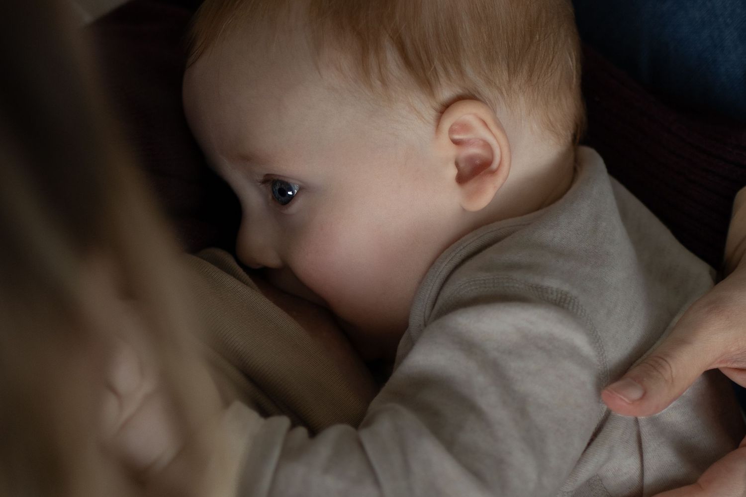 Close-up of breastfeeding infant in moody lighting against dark background.