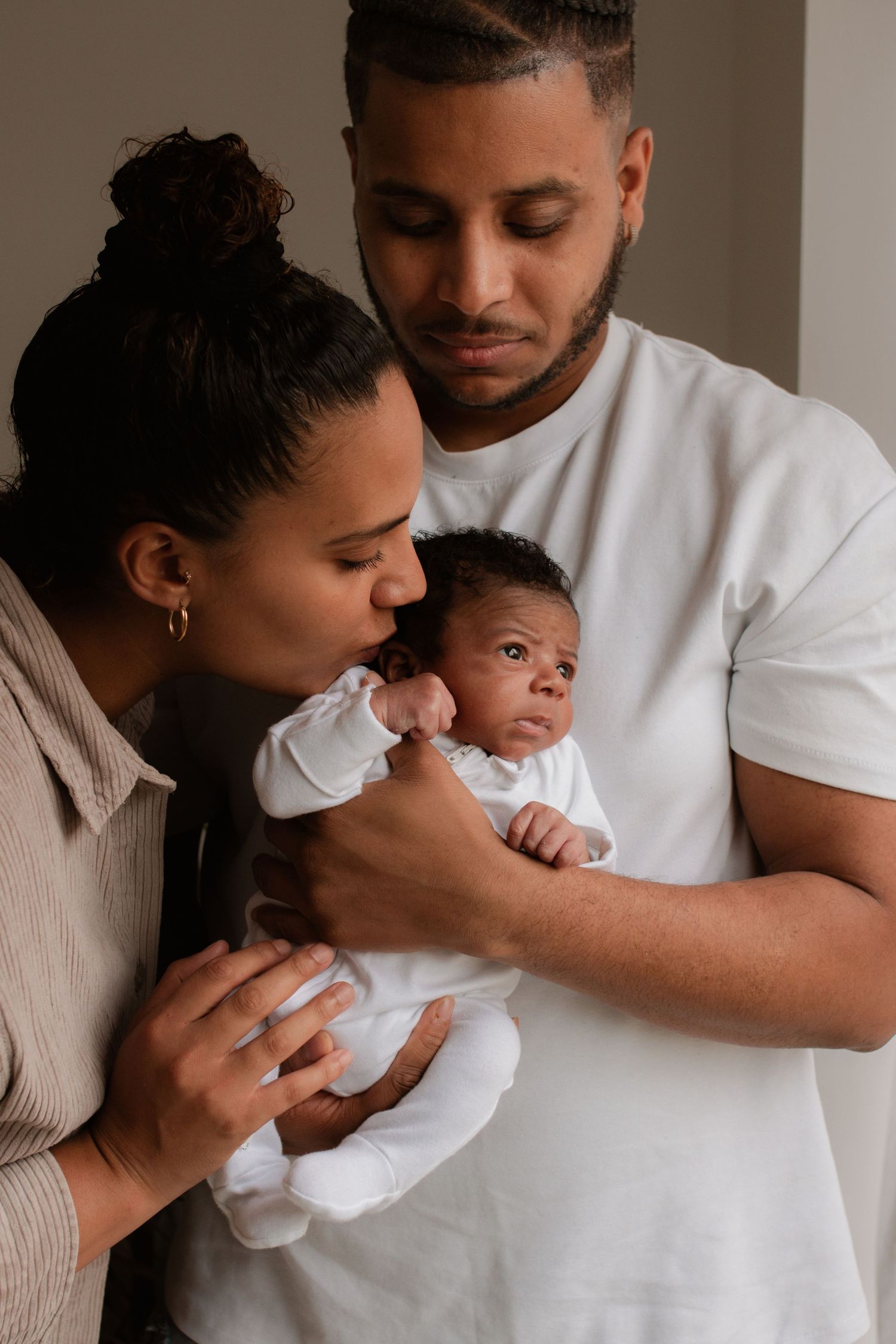 Family sharing intimate moment with newborn baby in minimalist setting.