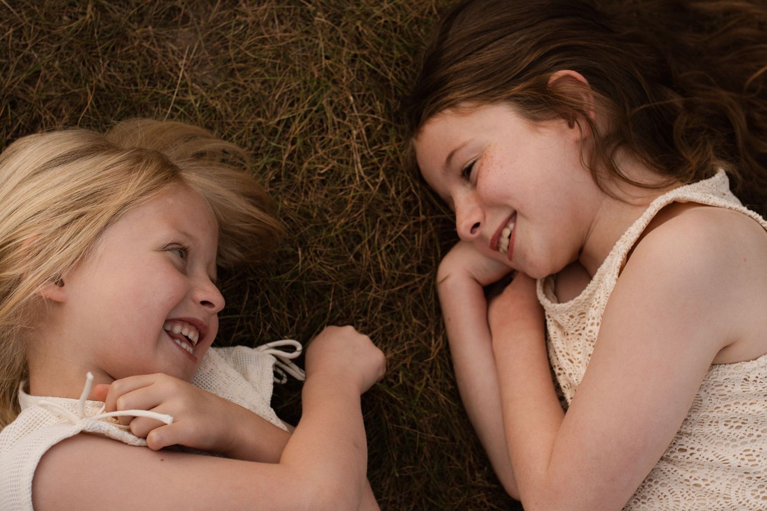Two young friends lying in grass and laughing together on a sunny day.