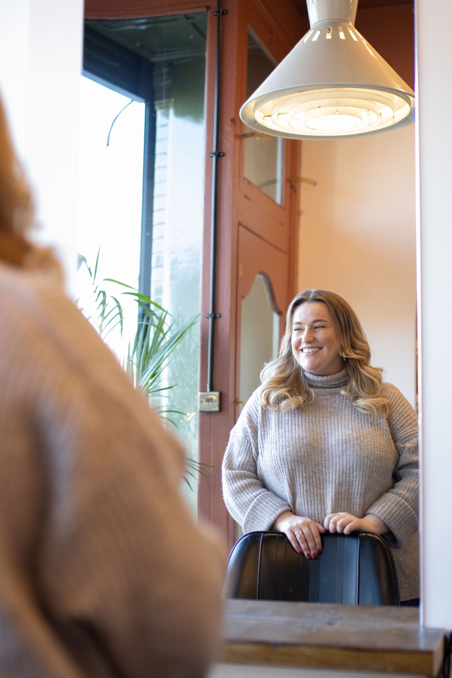 Person wearing gray sweater sitting by window in cafe with natural lighting.