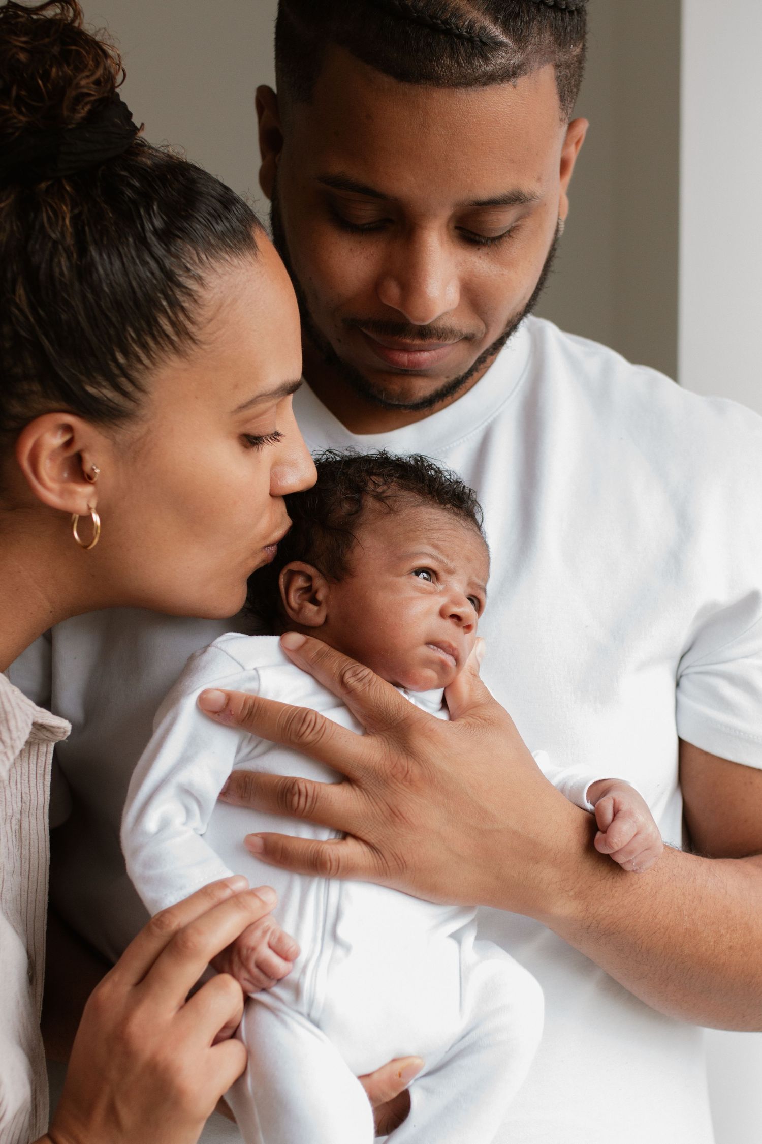 A series of tender moments between parents and their newborn baby wearing white against a neutral background.