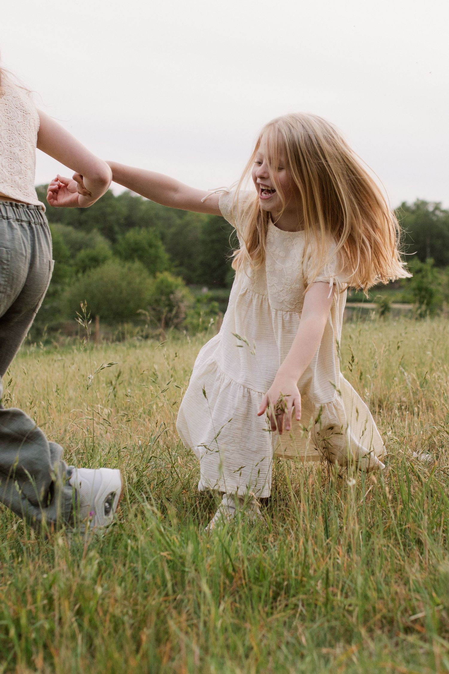 White dress flowing in the breeze as figures play in a summer meadow.