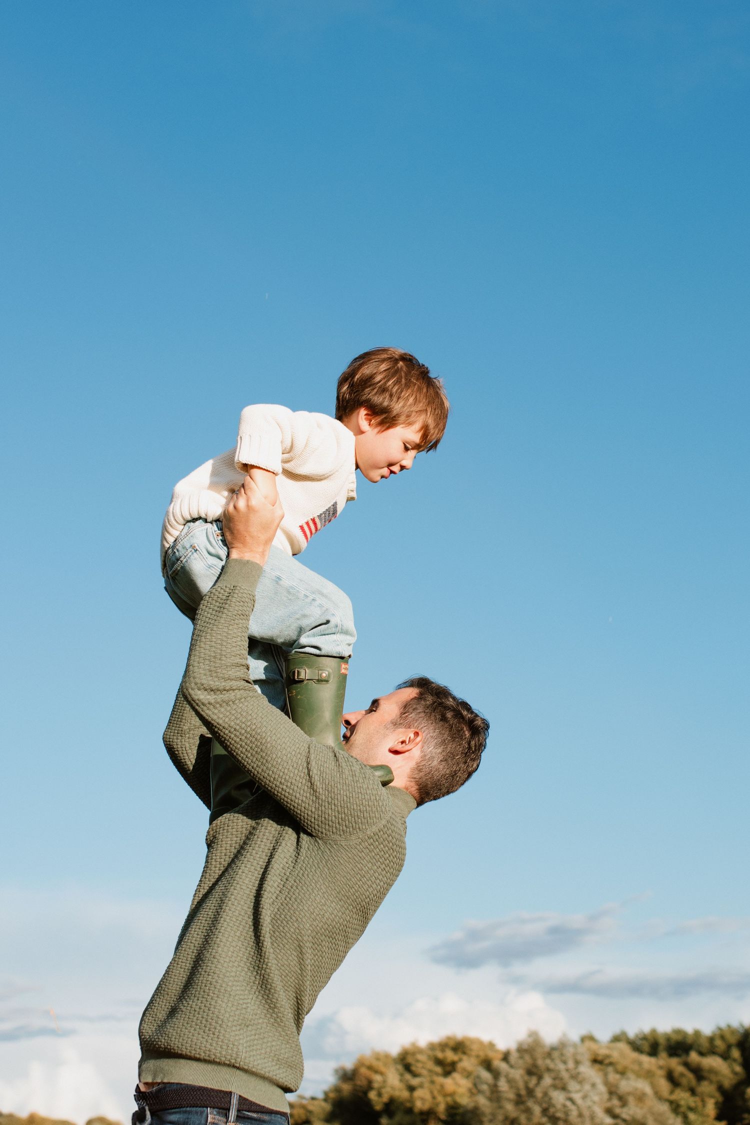 Joyful parent lifting child against bright blue sky outdoors.
