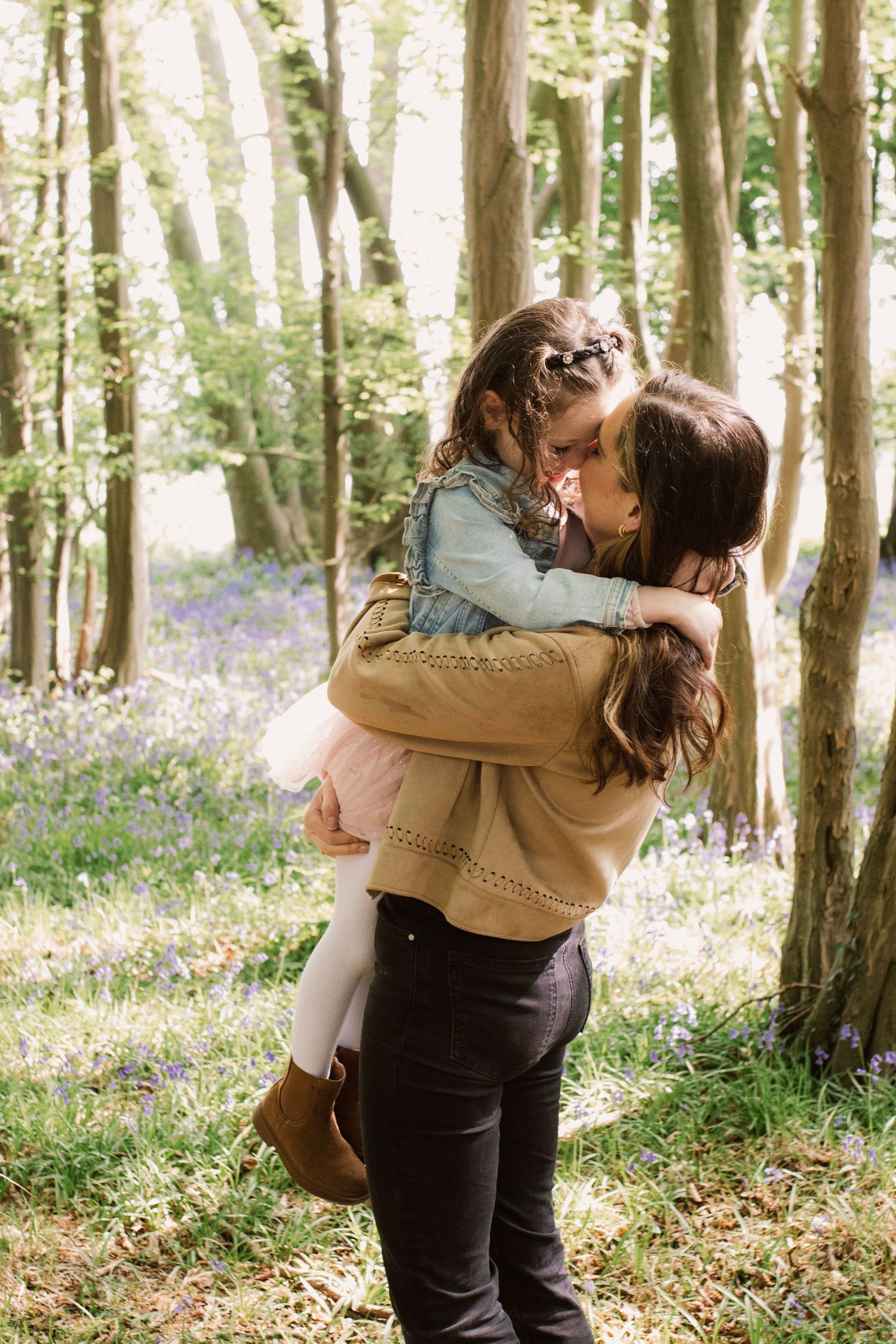 A tender embrace between two people in a sunlit forest filled with bluebells.