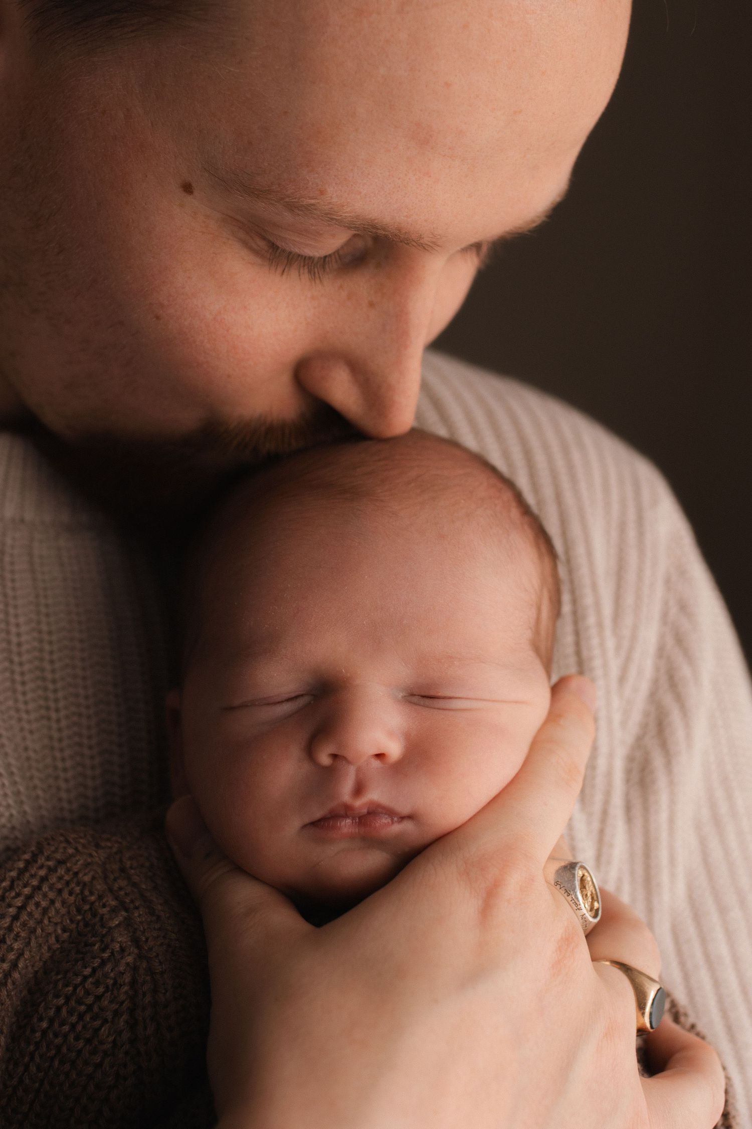 Tender moment between parent and sleeping newborn in soft natural light.