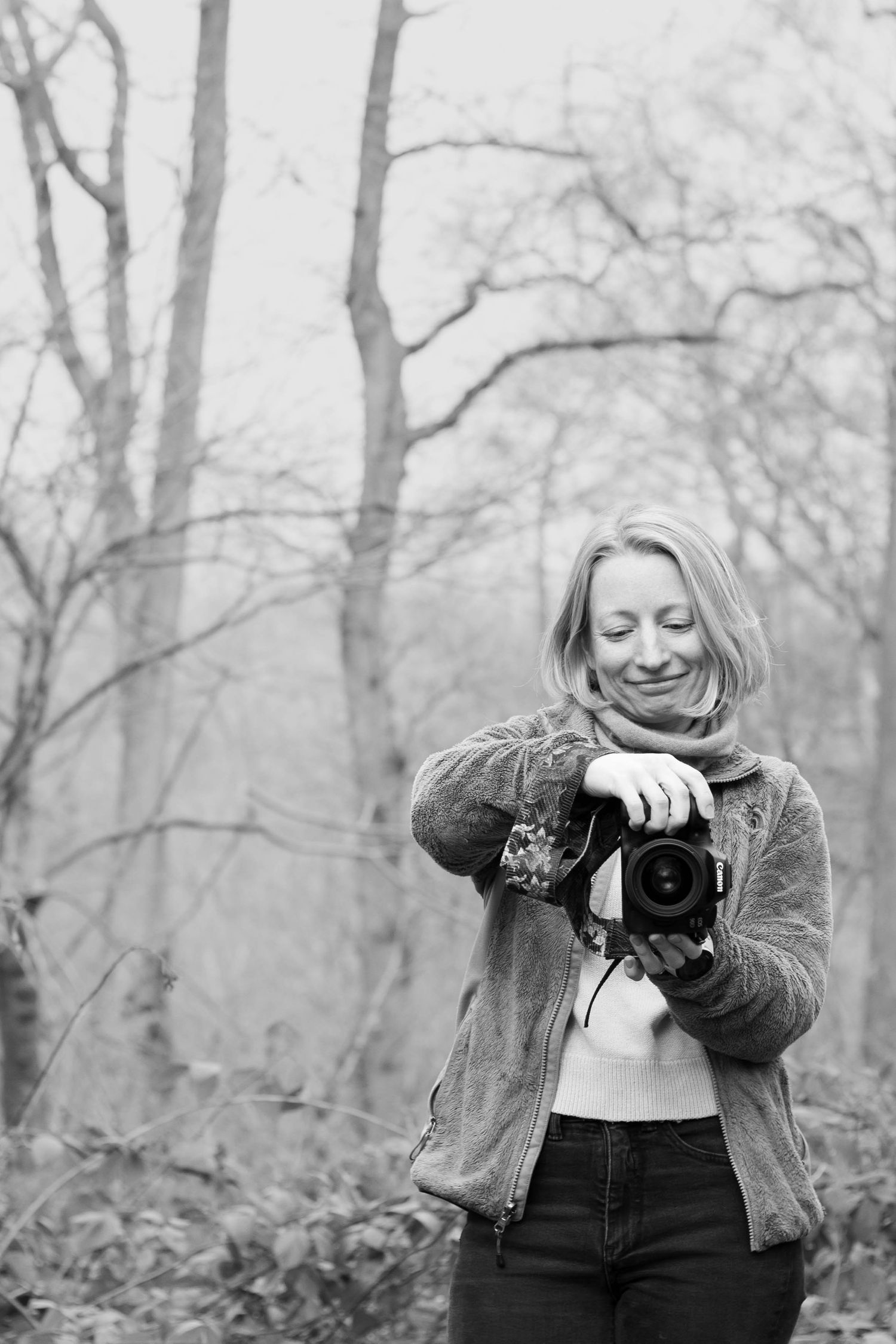 Black and white photo of photographer with camera in winter forest setting.