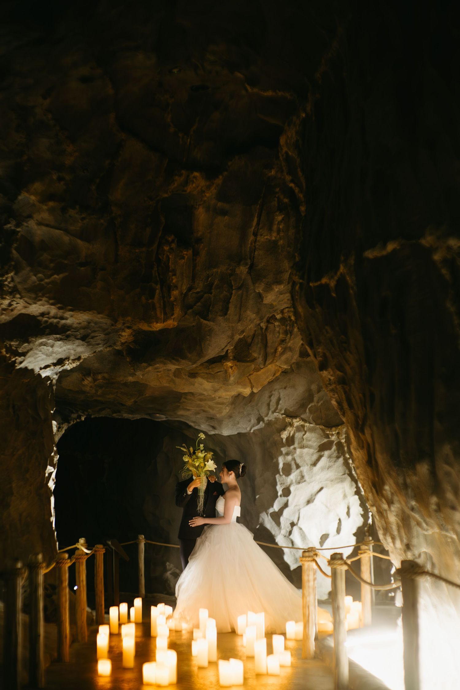 Illuminated cave with romantic candle decorations and person in a white tulle dress standing in the glow.