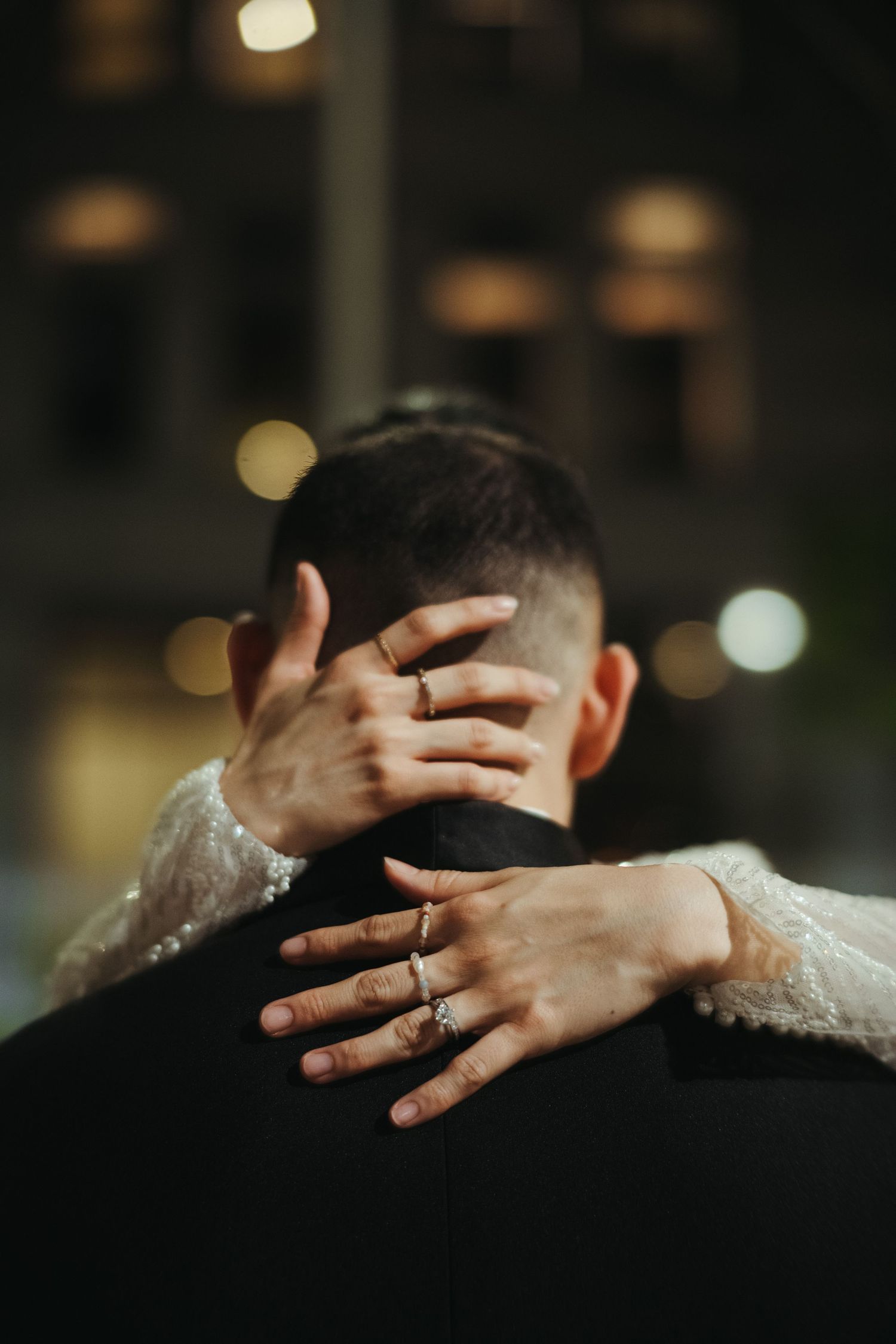Close-up of hands embracing during romantic moment with sparkling engagement ring and lace sleeve details.