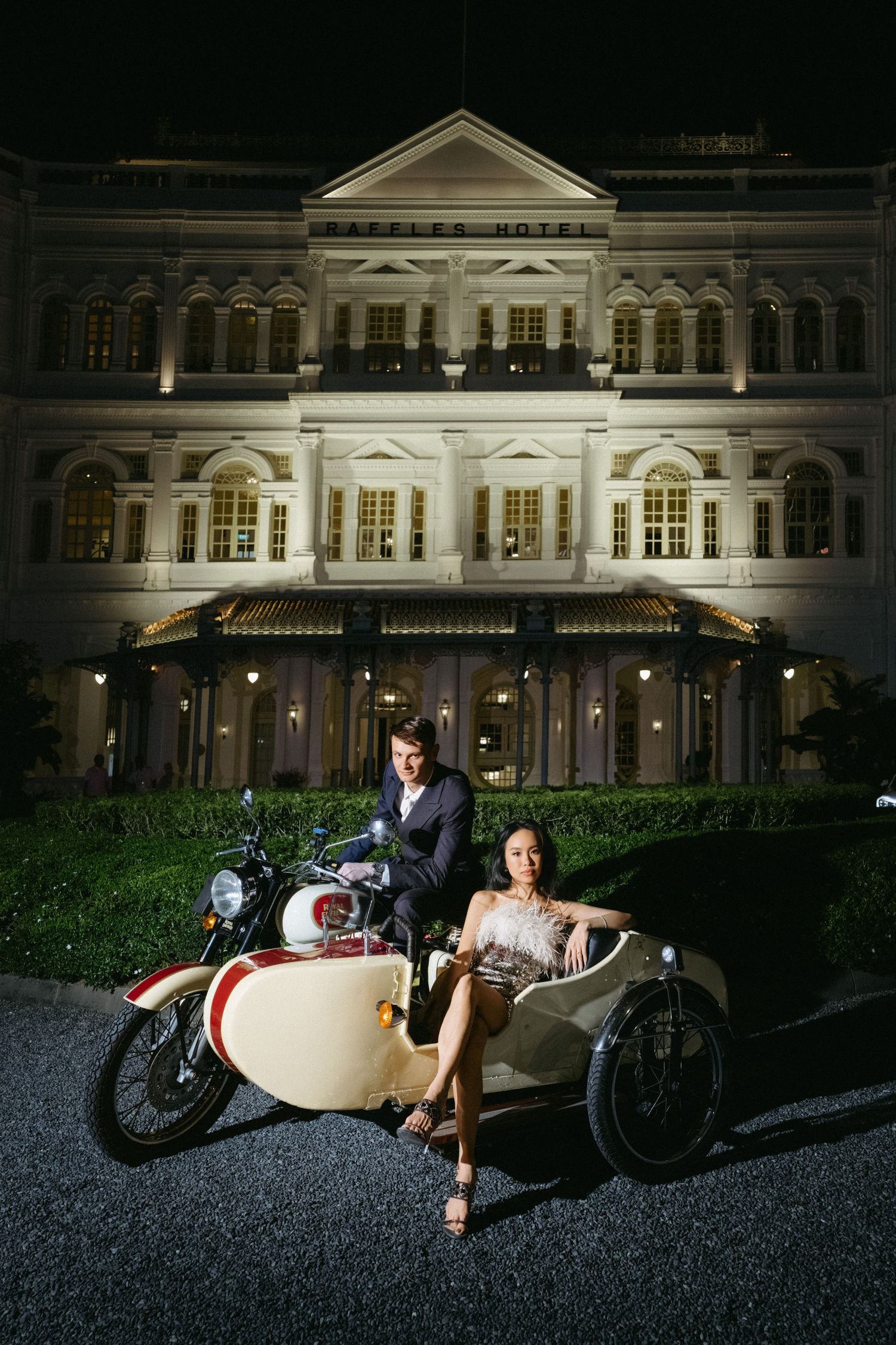 A romantic vintage motorcycle sidecar photoshoot at night in front of an illuminated historic mansion.