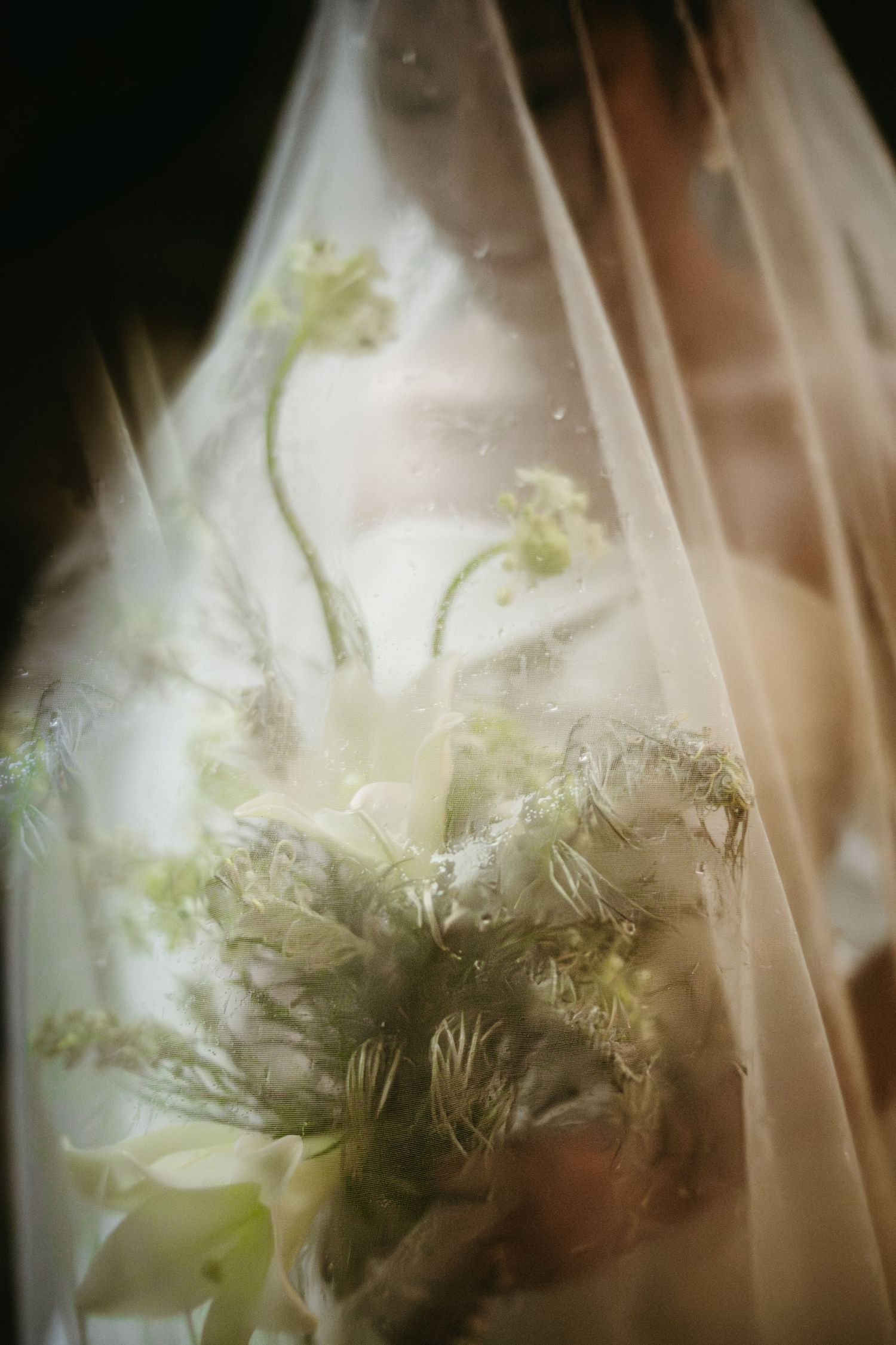 A dreamy and ethereal wedding photograph showing soft flowers behind a delicate veil with a romantic blurred effect.