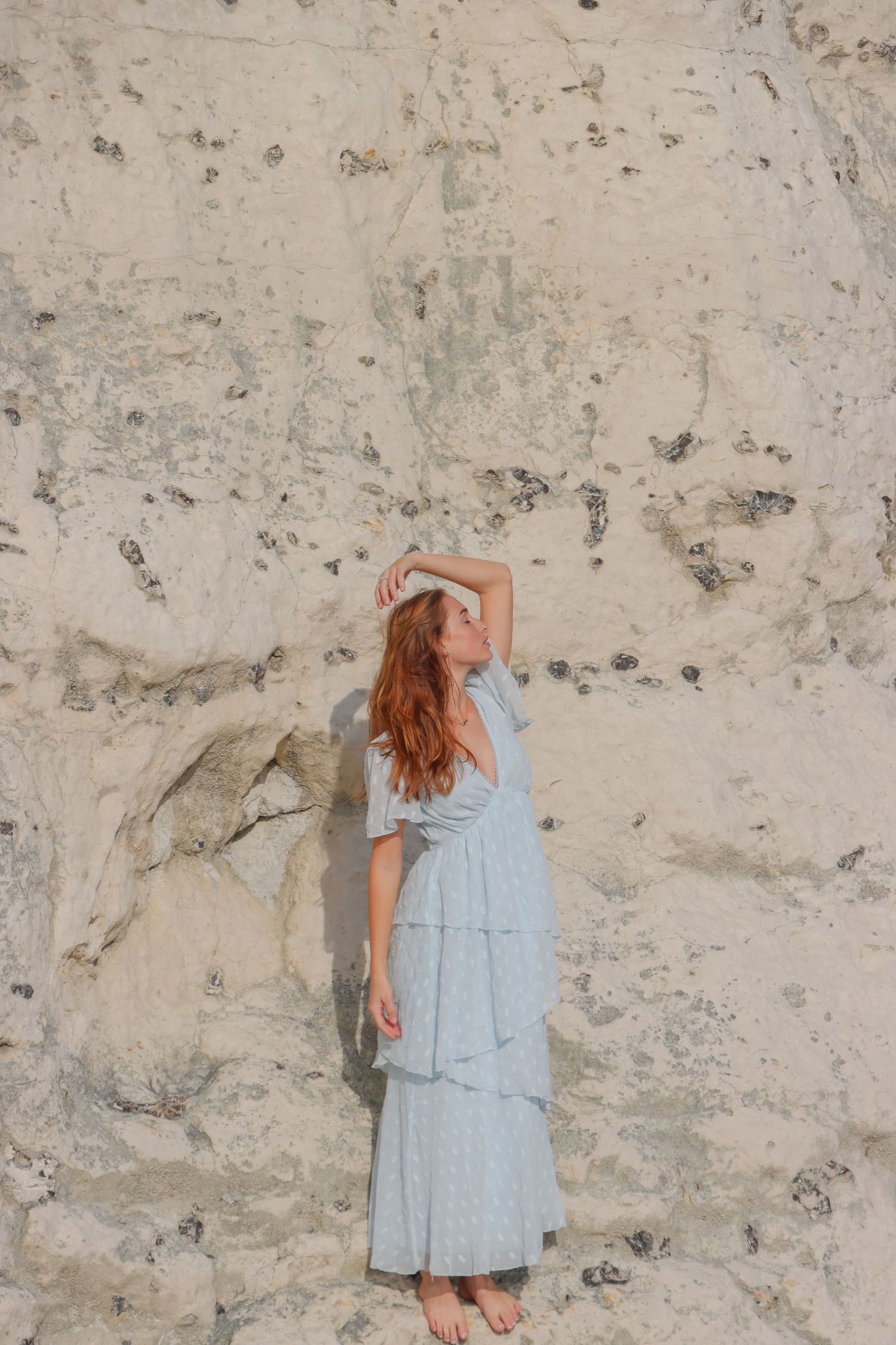Figure in light blue dress poses against textured stone wall in sequence. By Chrissie McLean Photography.