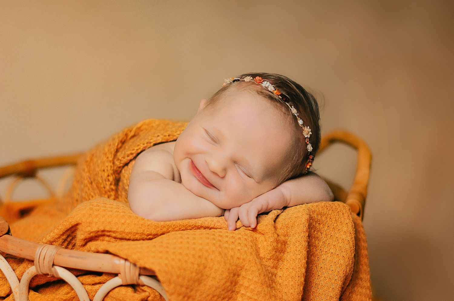 Sleeping baby wrapped in cozy orange knit blanket with delicate headband during professional newborn photoshoot. Nitro Photo