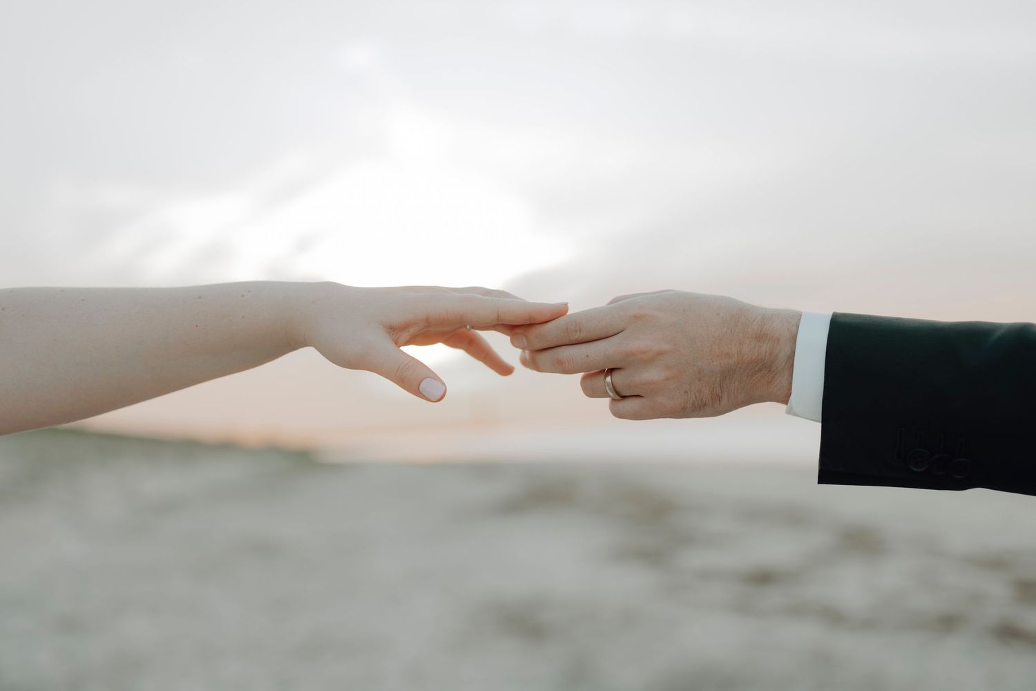 Two hands reaching toward each other with gentle tenderness against a soft, blurred background.
