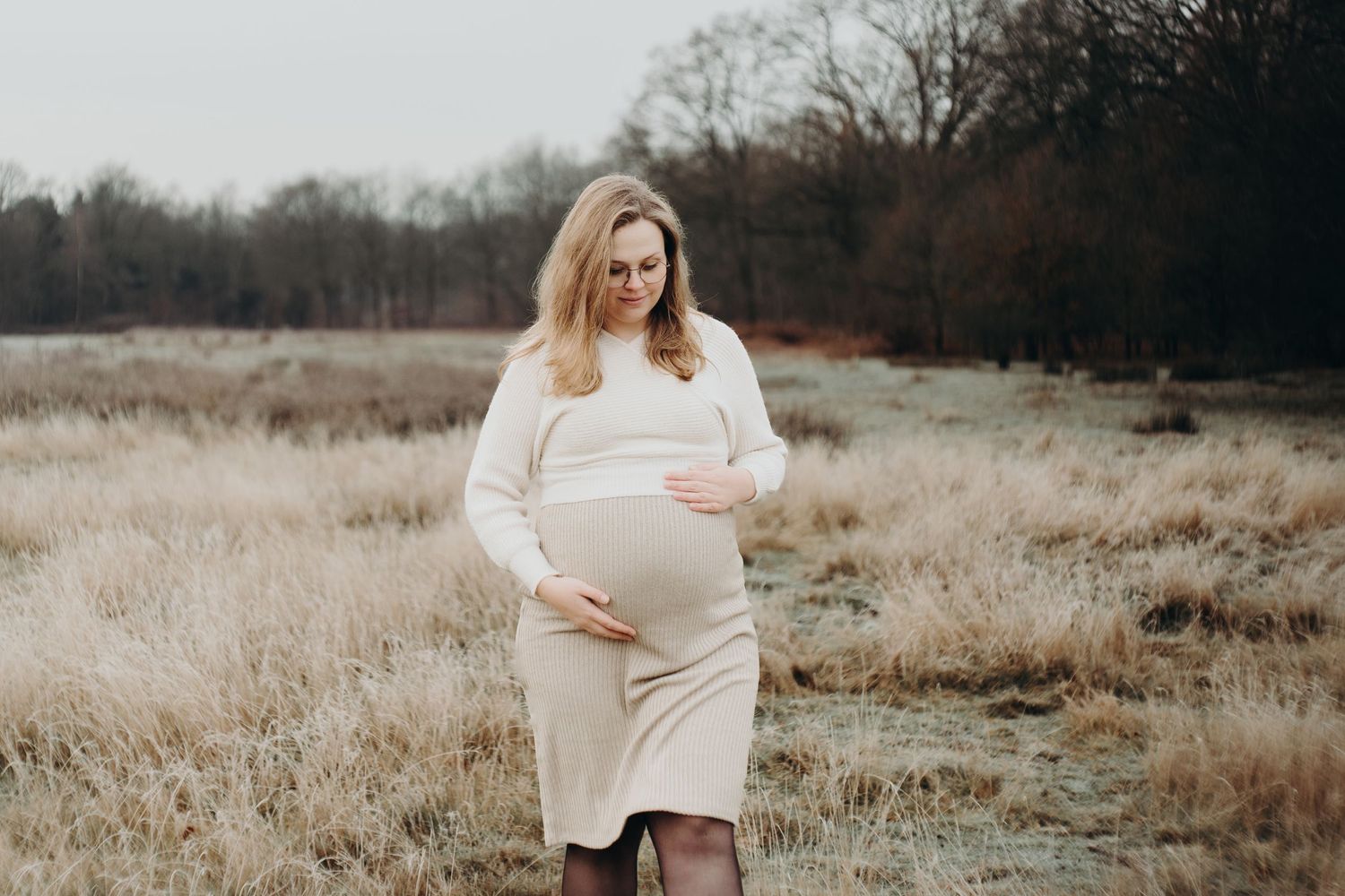Maternity photo of woman in white dress standing in golden autumn field.