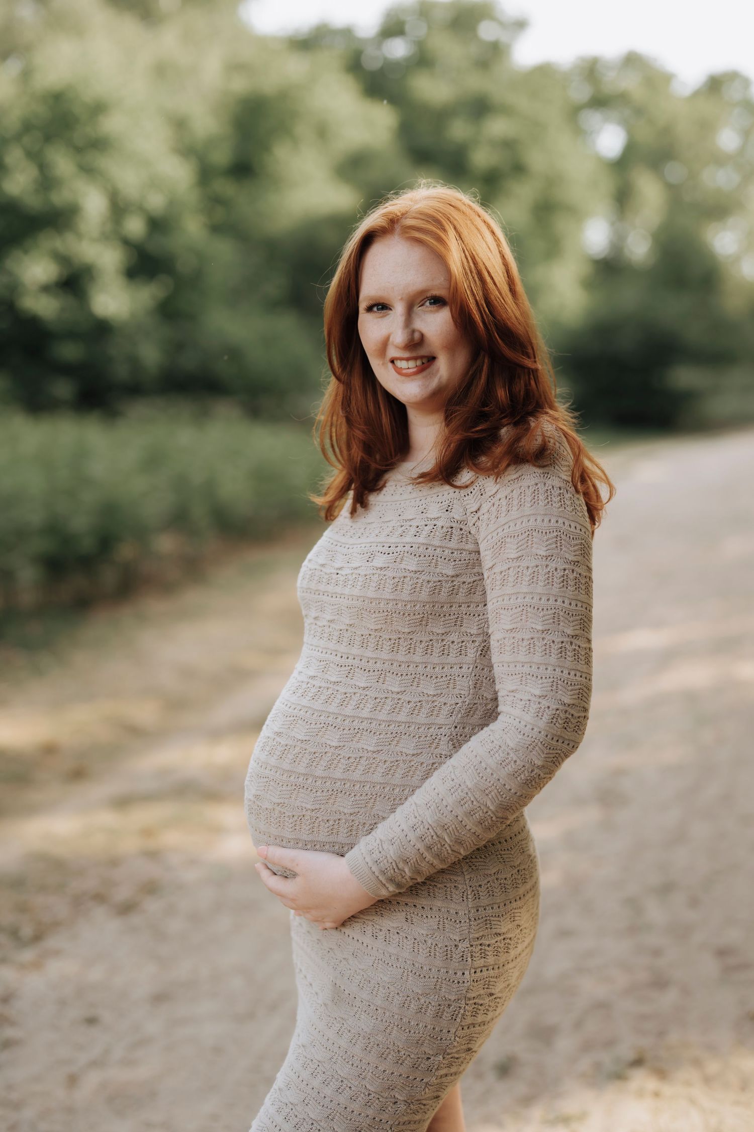 Someone in a cozy knit sweater dress poses outdoors on a nature path during a maternity photoshoot.