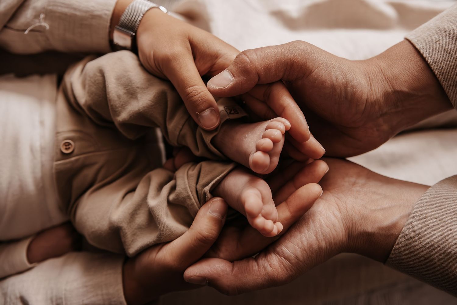 Close-up shot of hands tenderly holding each other against a beige fabric background.