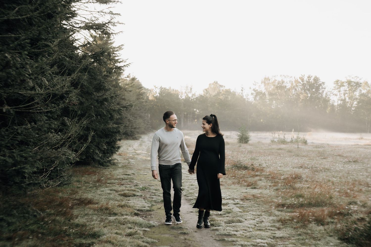 Couple walking together on foggy path beside evergreen trees.