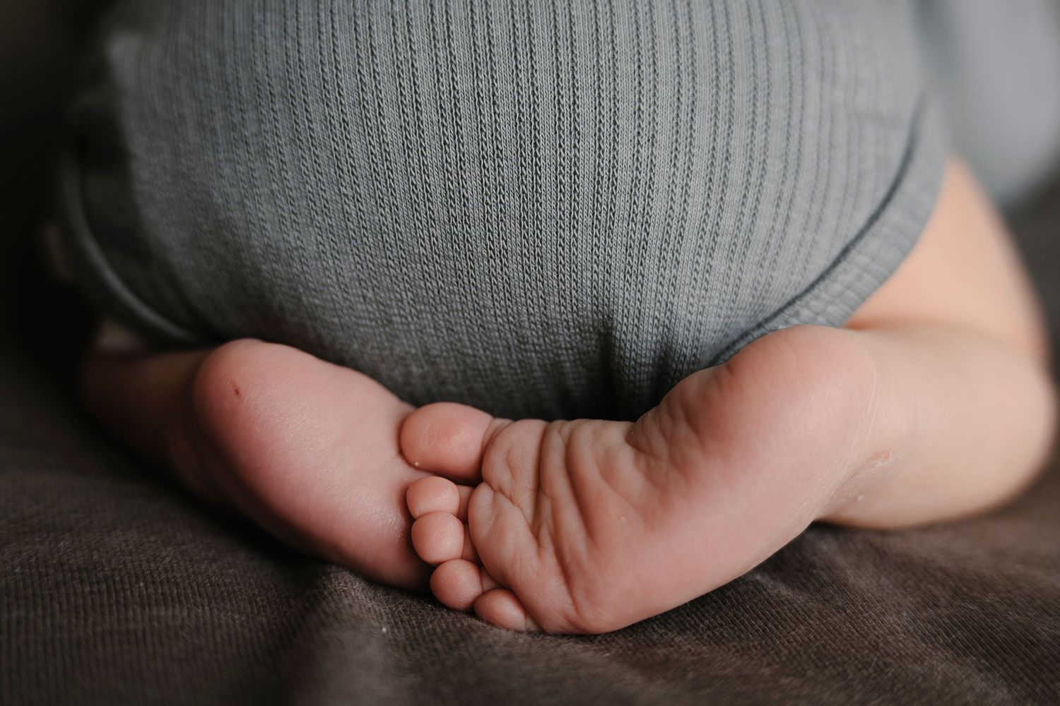 Close-up view of tiny baby feet in soft gray clothing against a dark textile background.