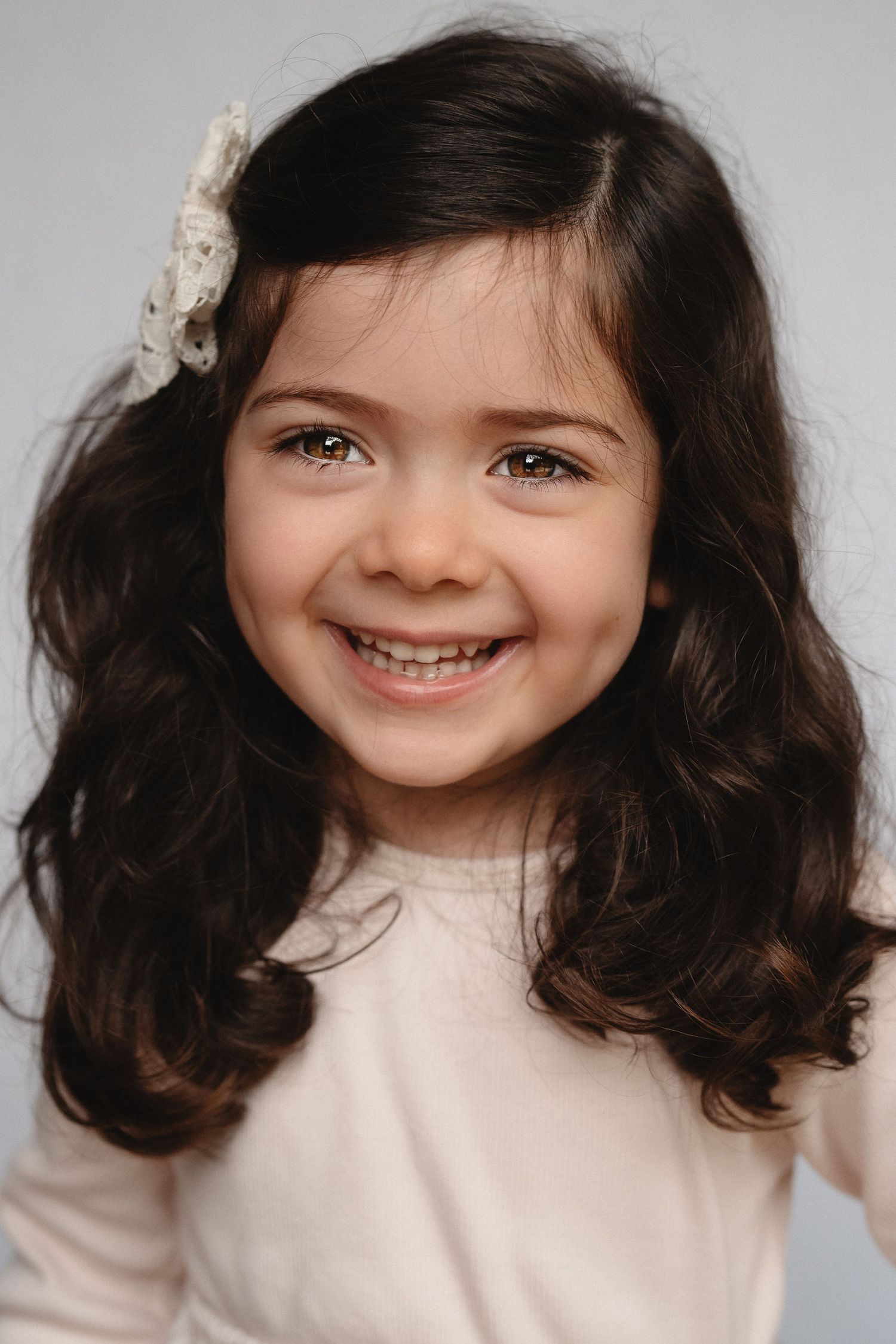 Studio portrait featuring bright smile and curly dark hair with white hair accessory.