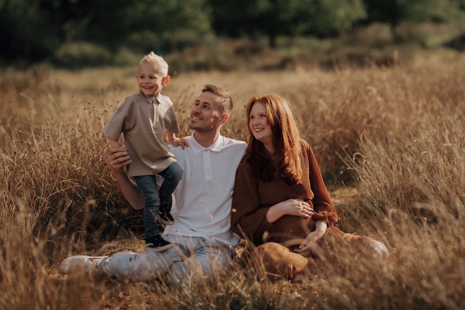 Loving family sits together in a golden sunlit meadow during a warm autumn afternoon.