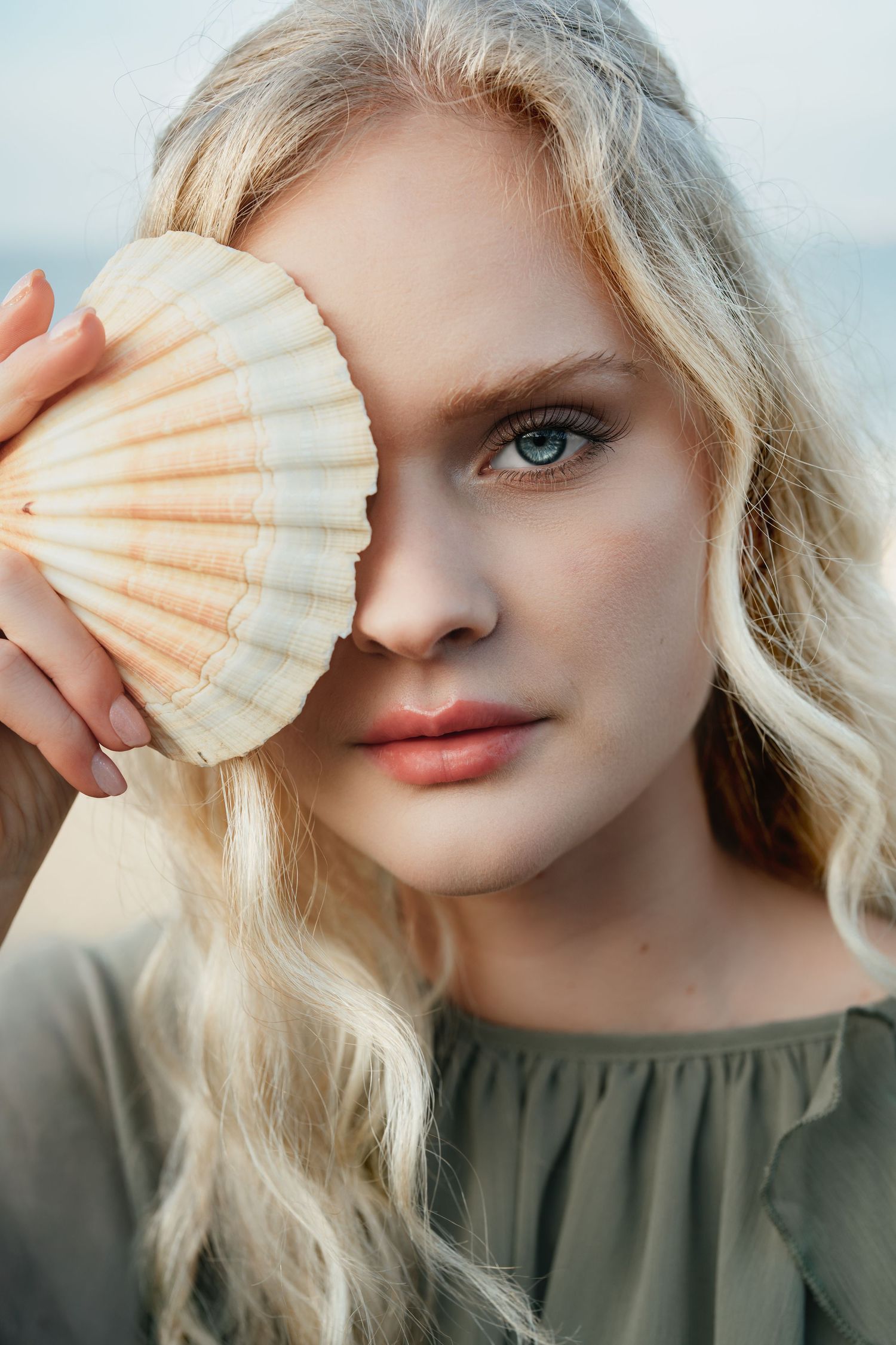 Artistic beauty portrait featuring a large seashell held against soft natural lighting.