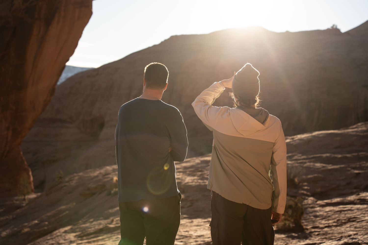 Two hikers stand facing a dramatic desert canyon landscape bathed in golden sunlight.