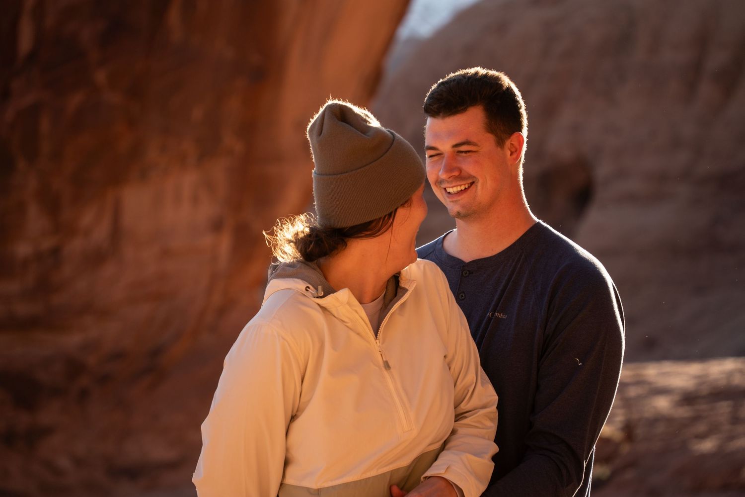 Couple smiling and sharing a romantic moment outdoors near red rock formations in warm golden light.