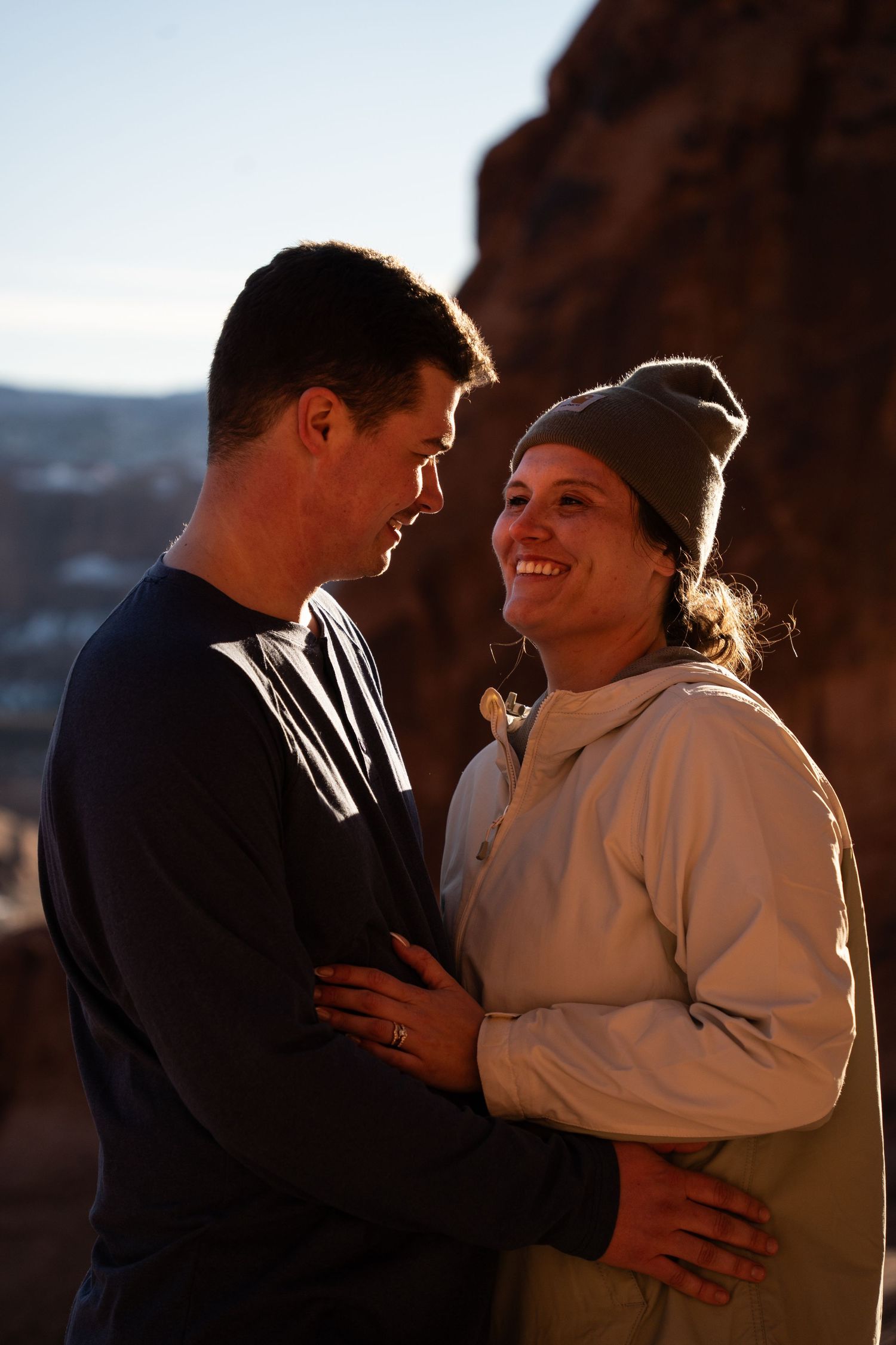 Couple embracing and smiling at sunset near red rock formations in southern Utah after hiking proposal