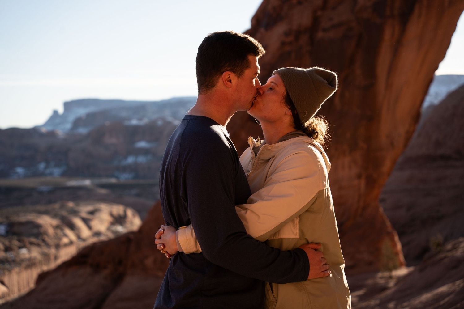 Couple sharing a romantic kiss in front of red rock canyon formations during golden hour after their proposal