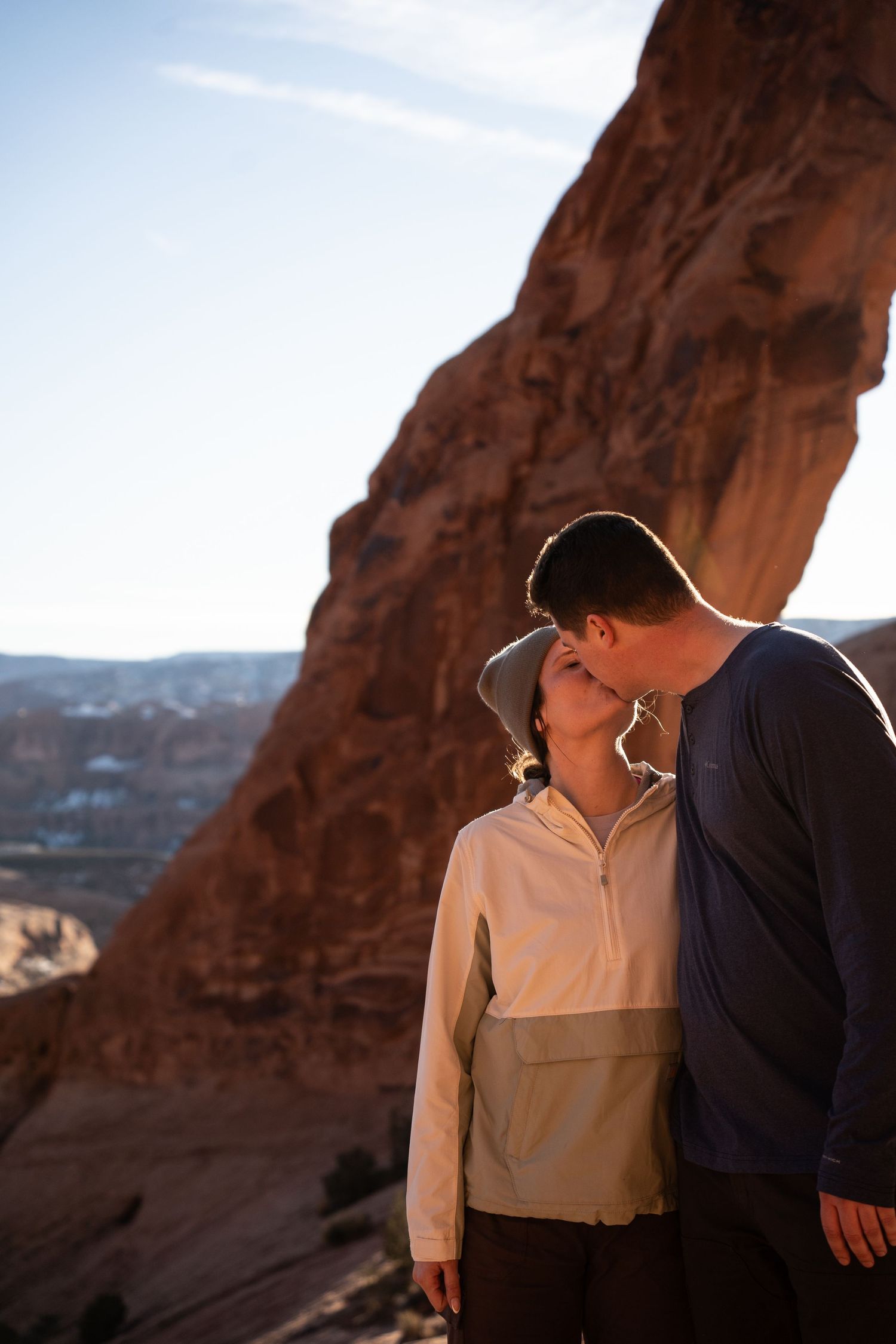 Couple sharing a romantic kiss against red rock canyon formations in golden hour sunlight.