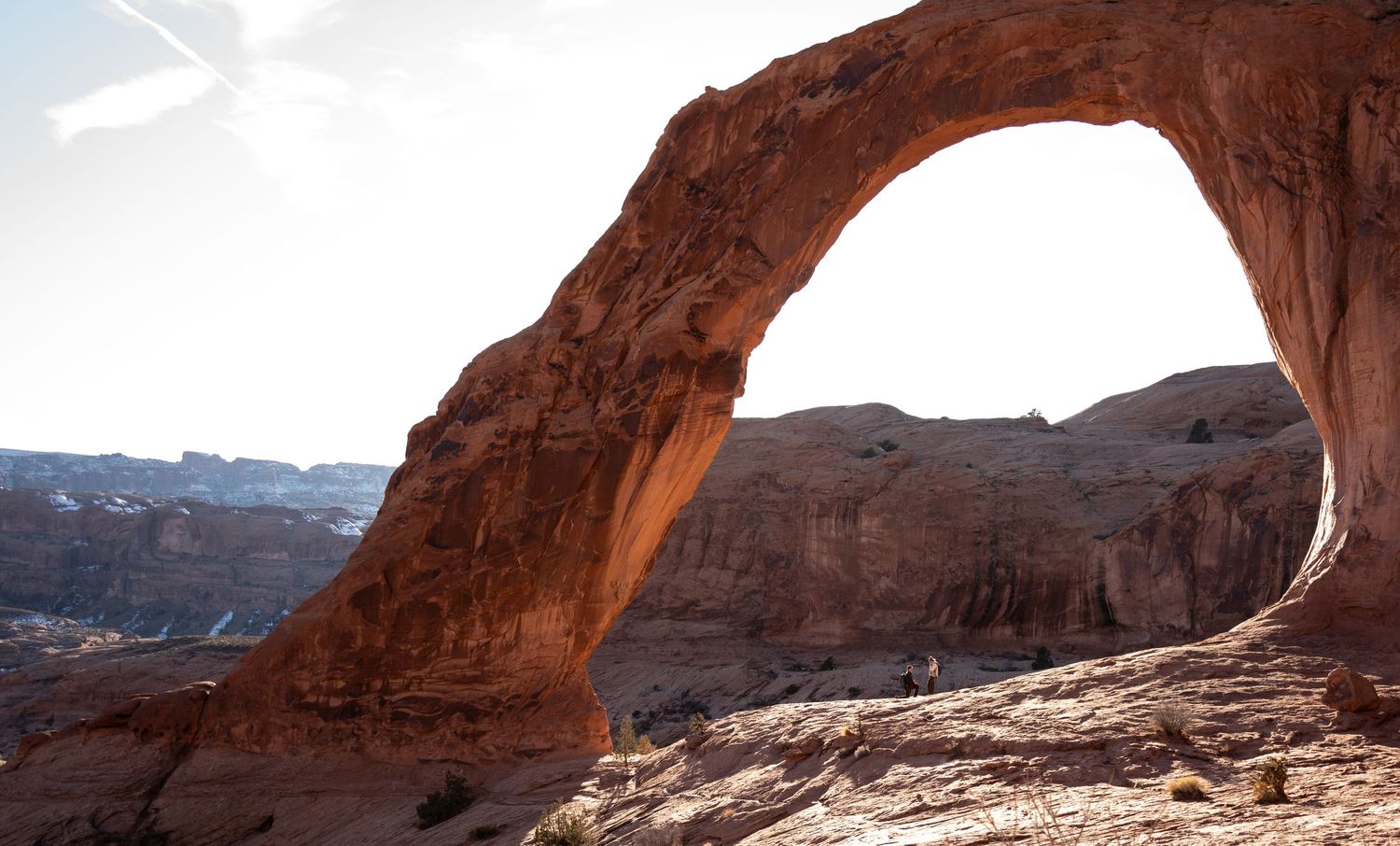 Massive red sandstone arch frames canyon landscape under bright sky at Arches National Park, Utah