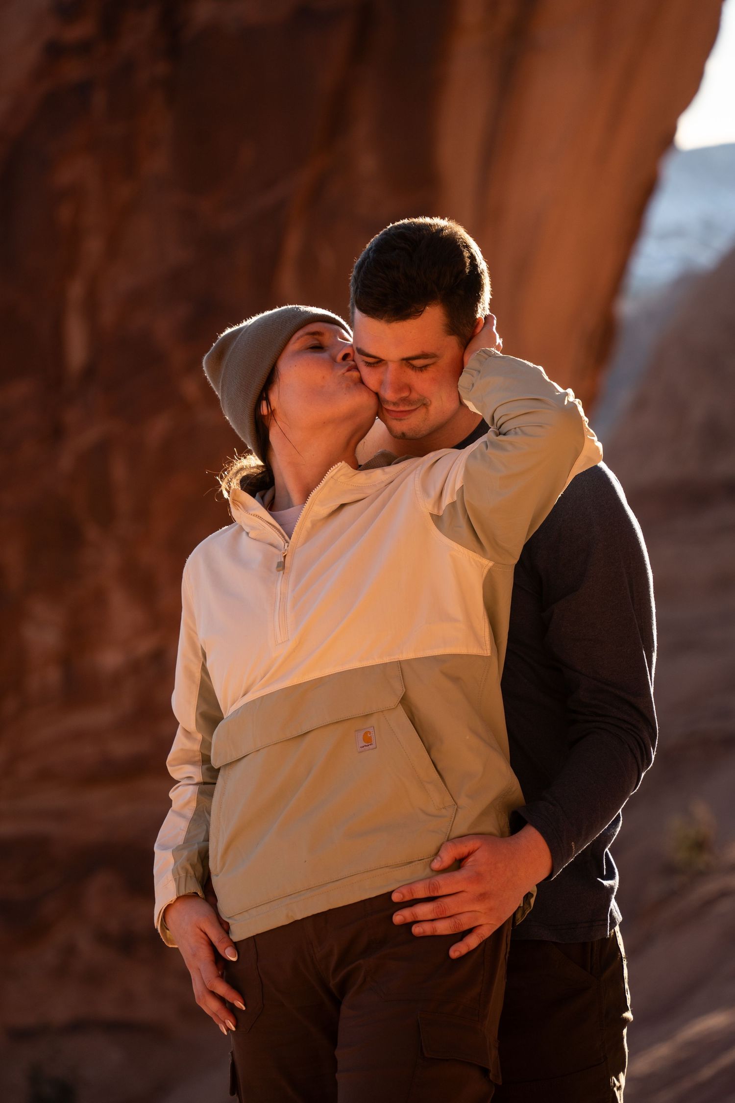 Couple sharing a romantic kiss outdoors near a red rock formation in warm golden light after romantic outdoors proposal