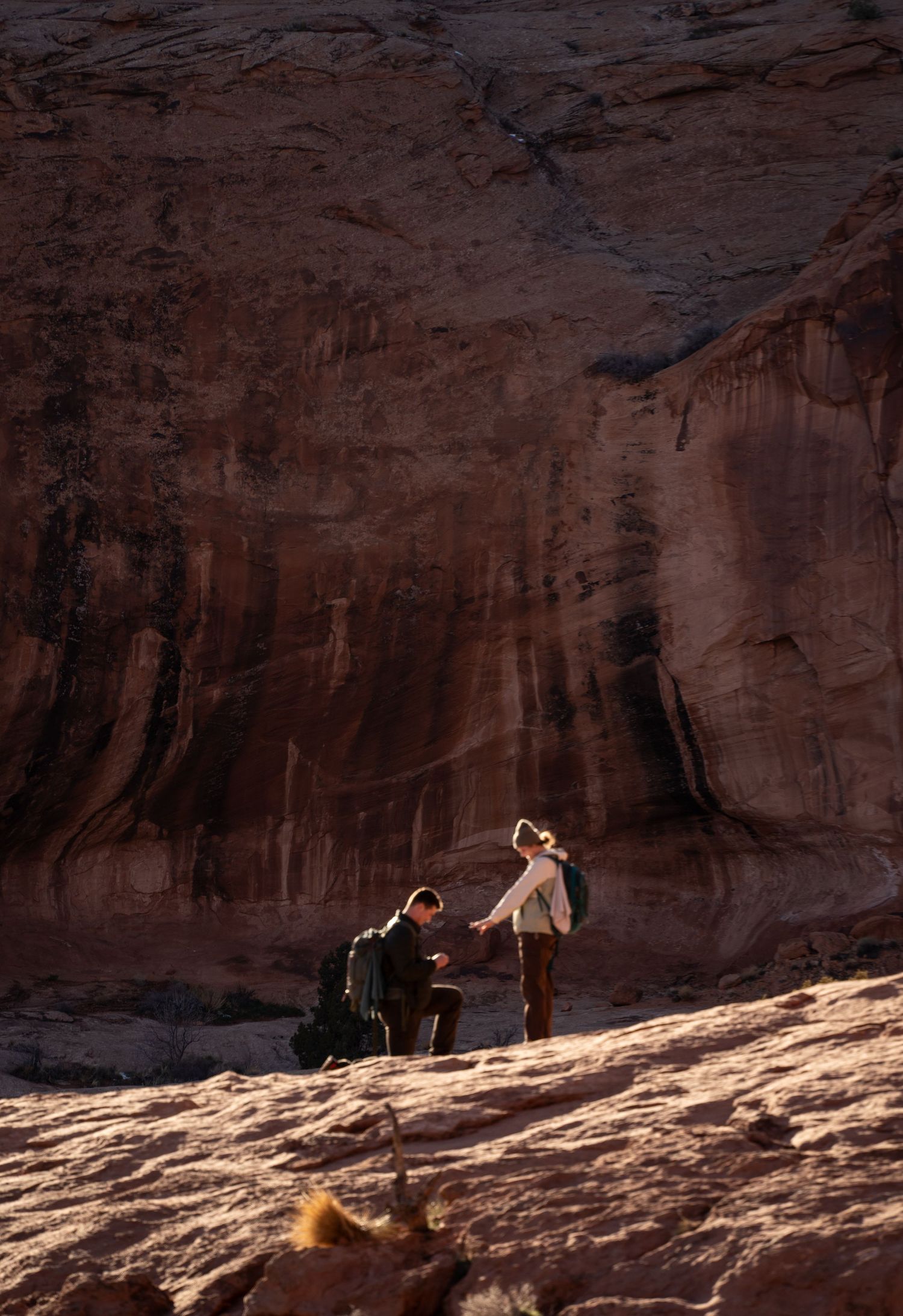 A romantic marriage proposal at corona arch moab utah, with a man on one knee before a woman against stunning sandstone cliffs.