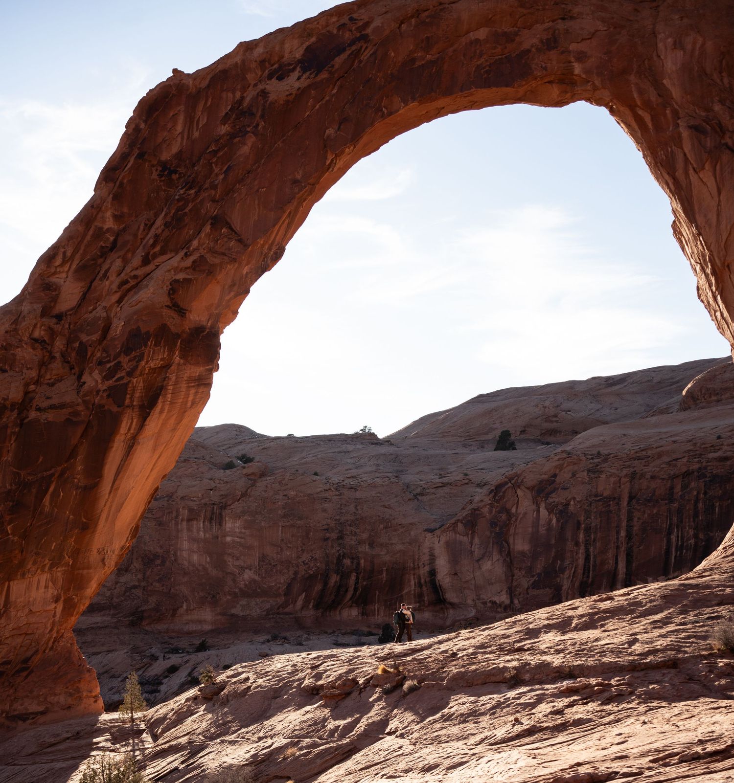 A massive red sandstone arch frames rocky desert landscape under a blue sky at Arches National Park, Utah with a proposal underneath