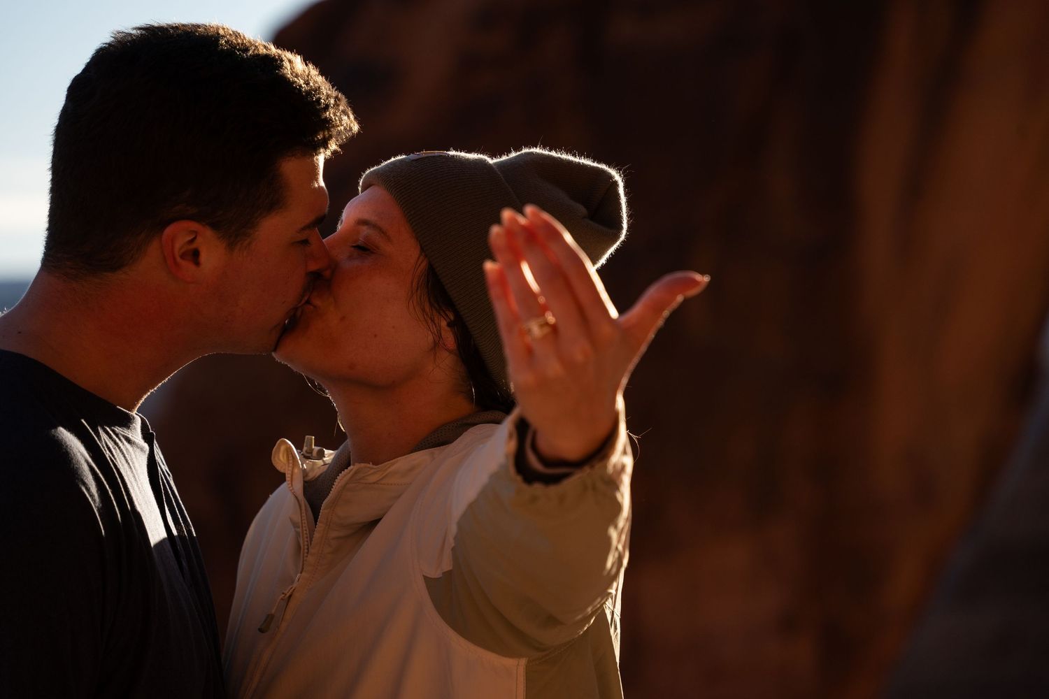 Couple sharing a romantic kiss after proposal, woman showing engagement ring on her hand.